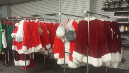 A bunch of santa claus costumes are hanging on racks in a store.