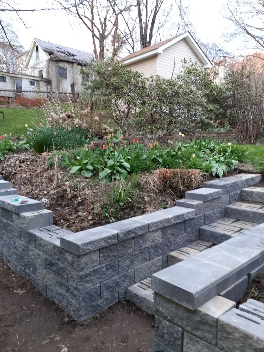 Raised garden bed with gray stone retaining walls and green plants in a residential yard