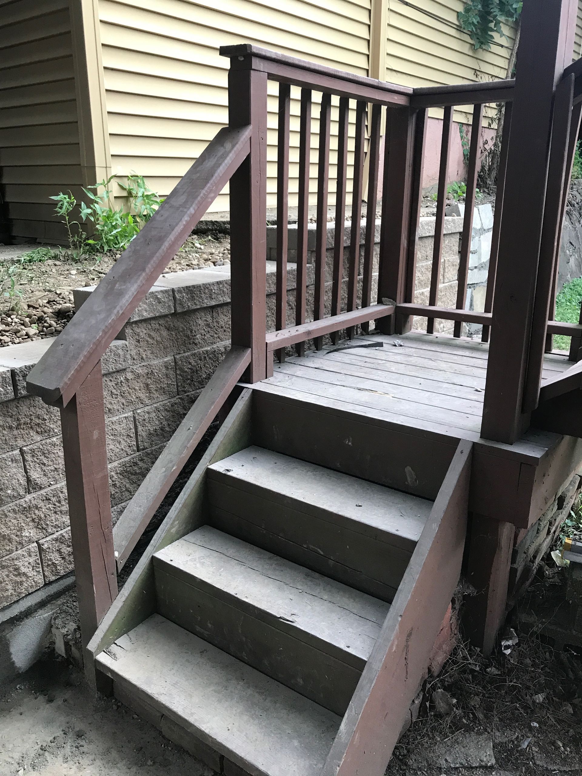 Wooden outdoor stairway with railings leading to a raised porch beside a house