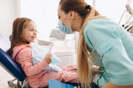 A little girl is sitting in a dental chair talking to a dentist.