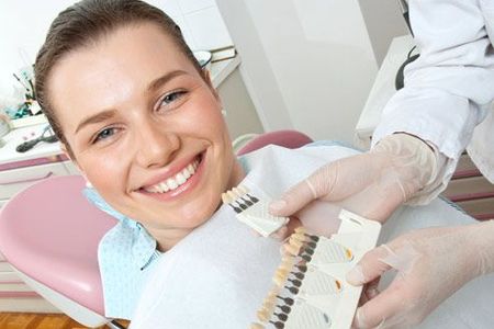 A woman is smiling while sitting in a dental chair while a dentist holds a model of her teeth.