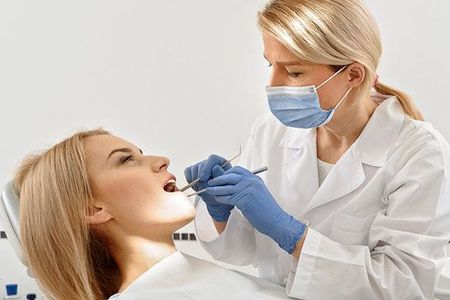 A female dentist is examining a woman 's teeth in a dental chair.