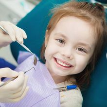 A little girl is smiling while getting her teeth examined by a dentist.