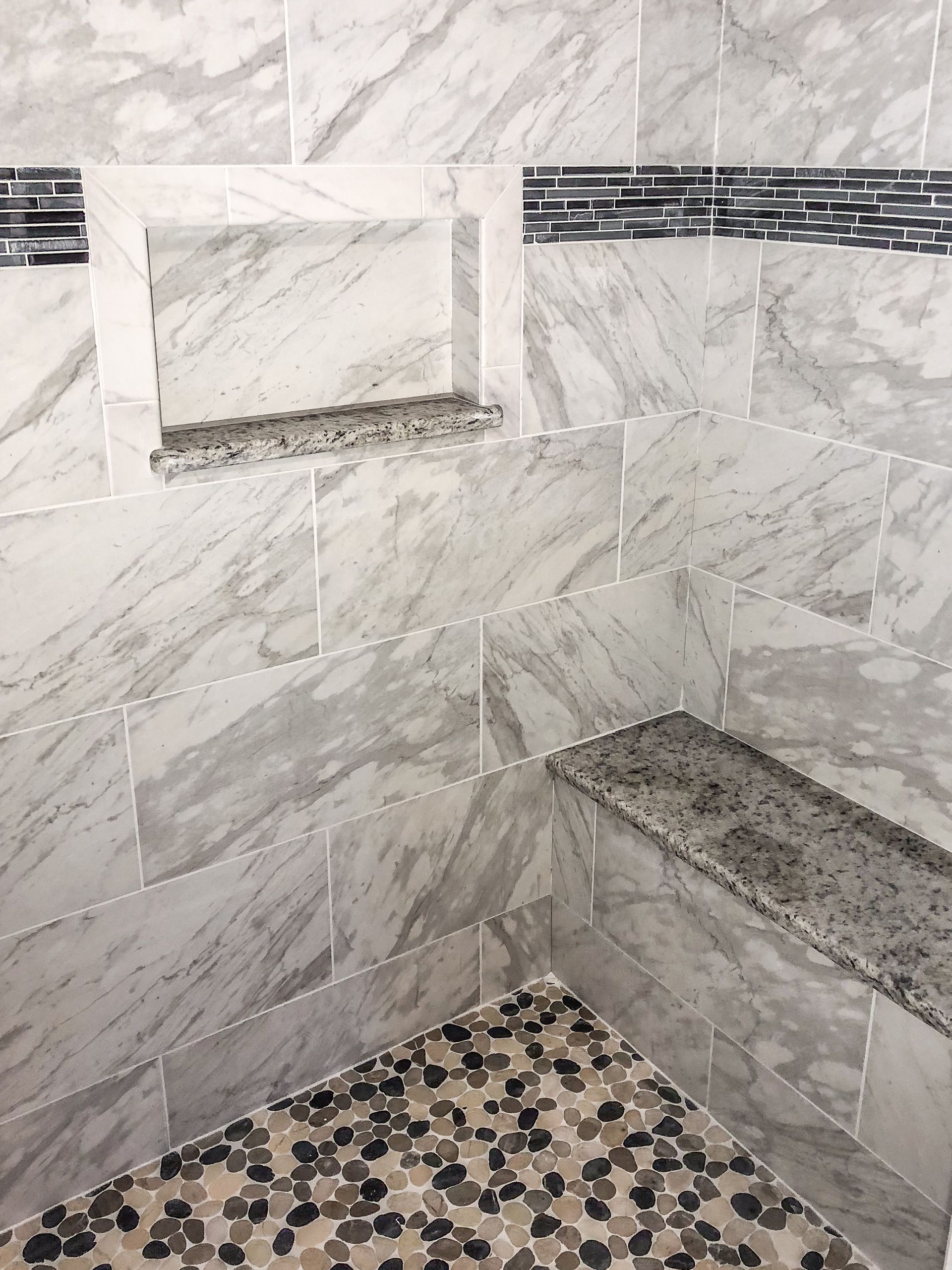 a shower with marble tiles and a bench in it