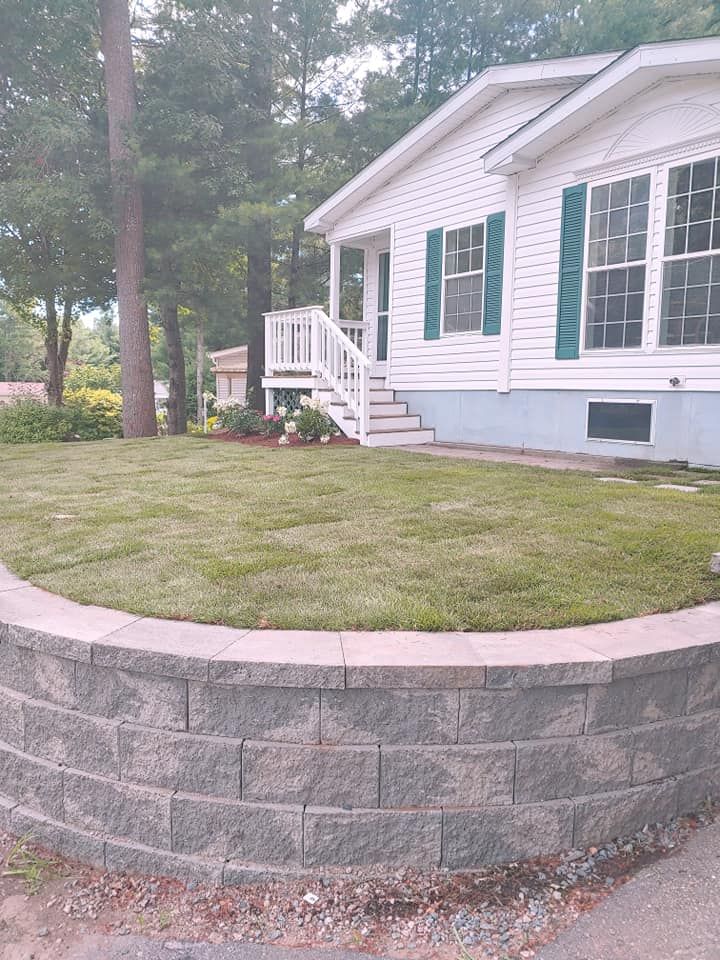 A white mobile home with green shutters and a brick wall in front of it