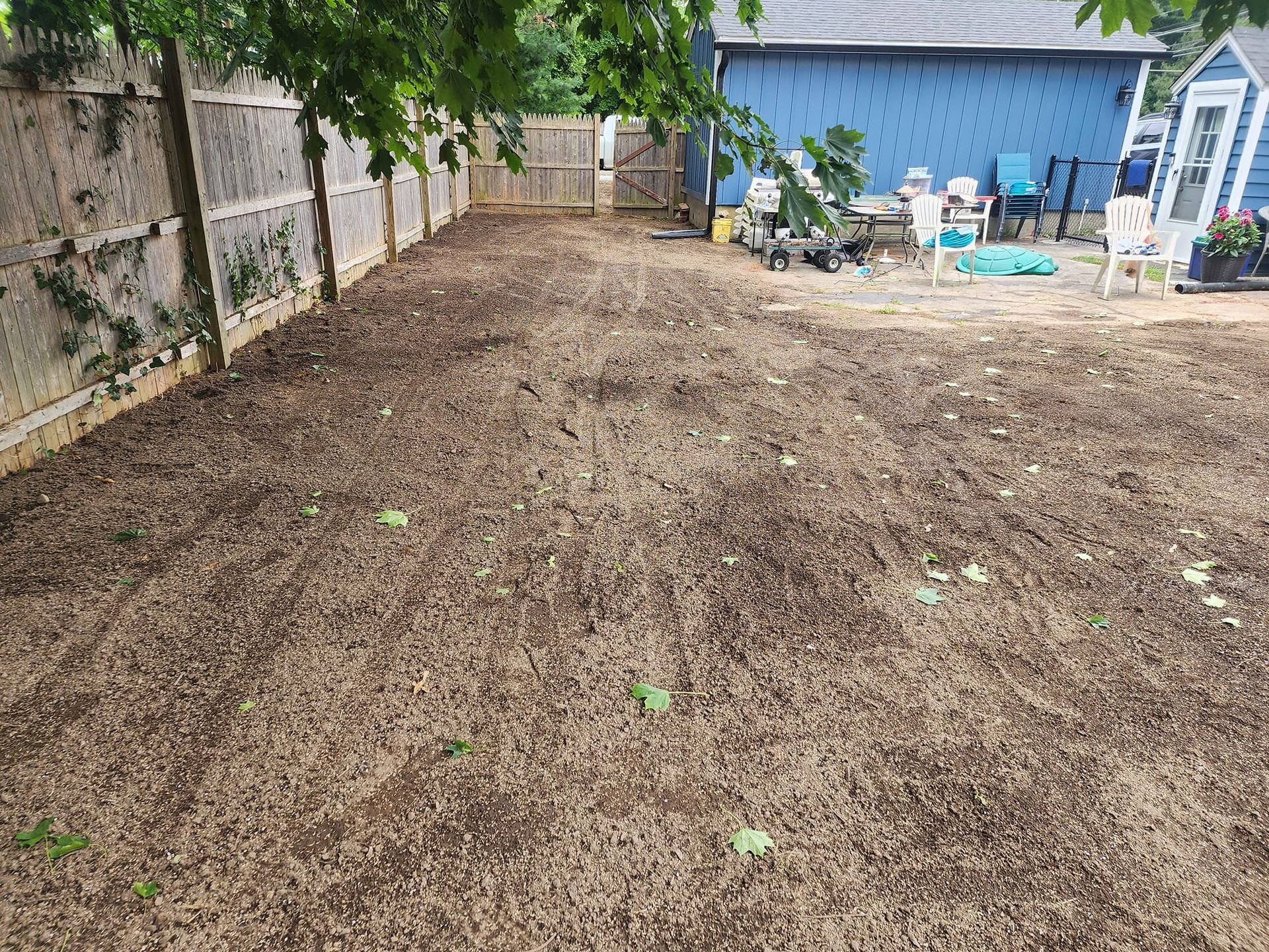 A backyard with a fence and a blue house in the background.