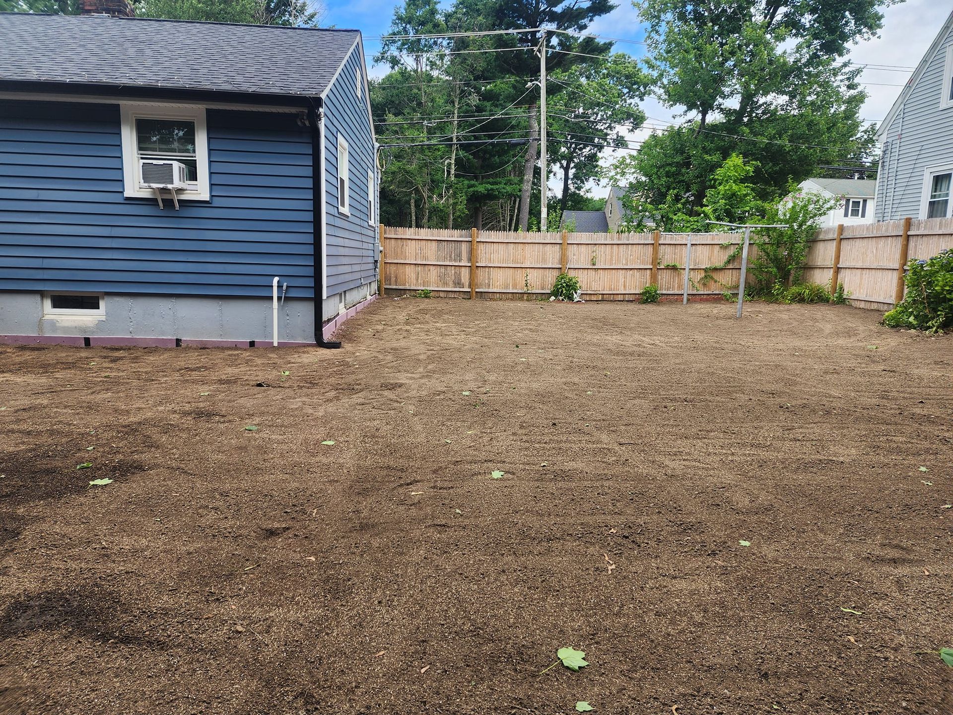 A blue house with a wooden fence and a lot of dirt in front of it.