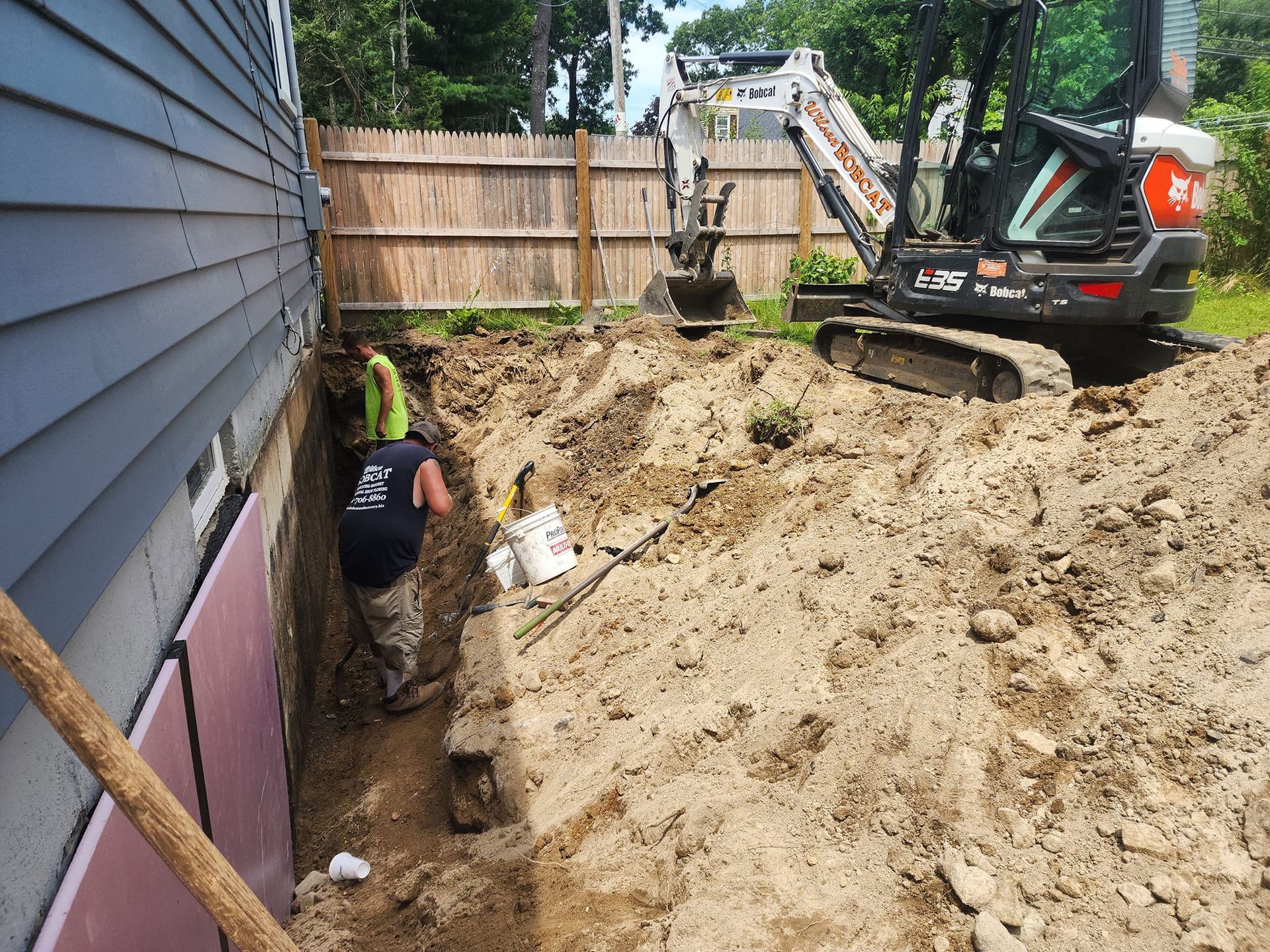 A man is digging a hole next to a house with a bulldozer in the background.