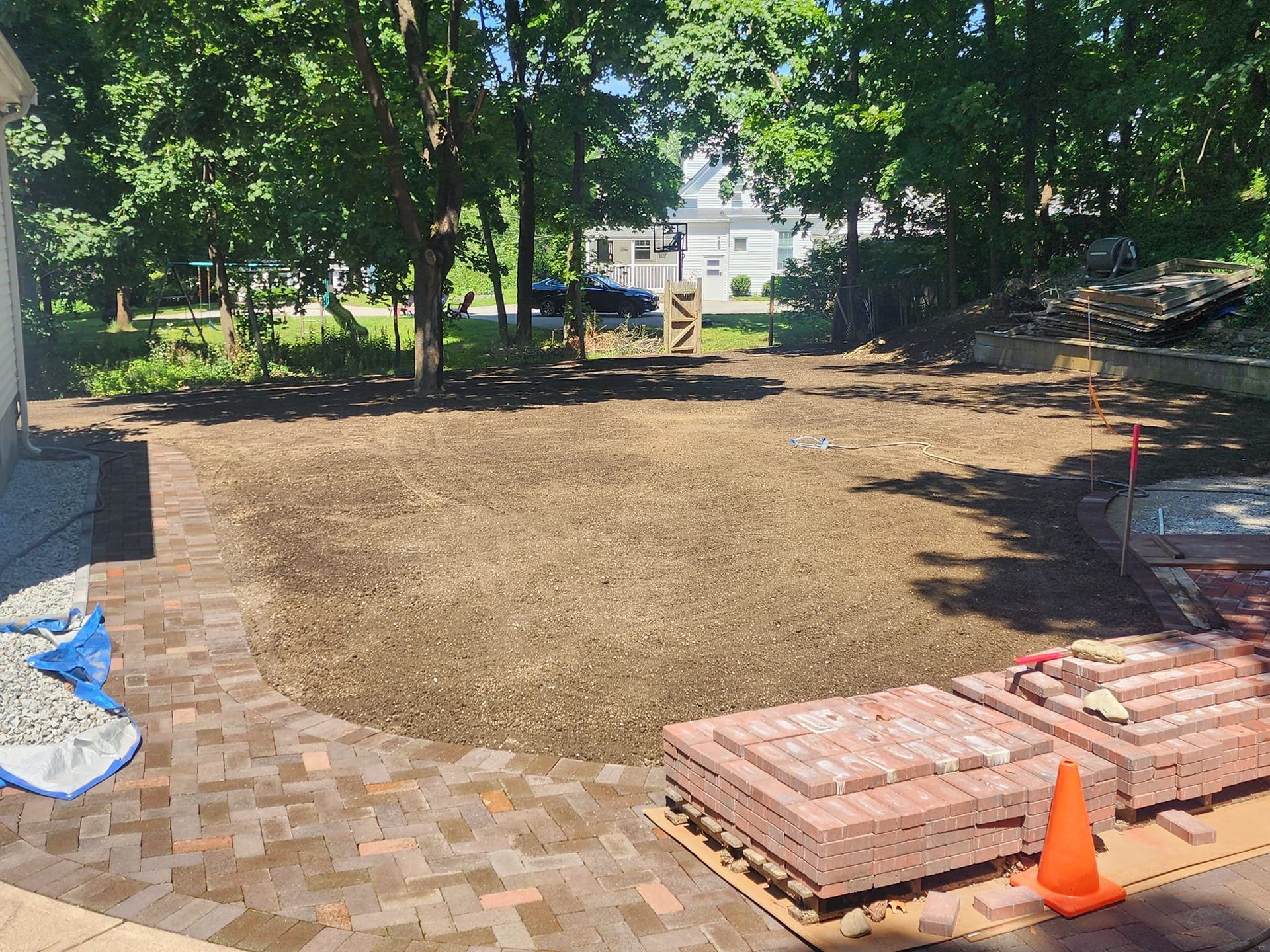 A brick patio is being built in the backyard of a house.