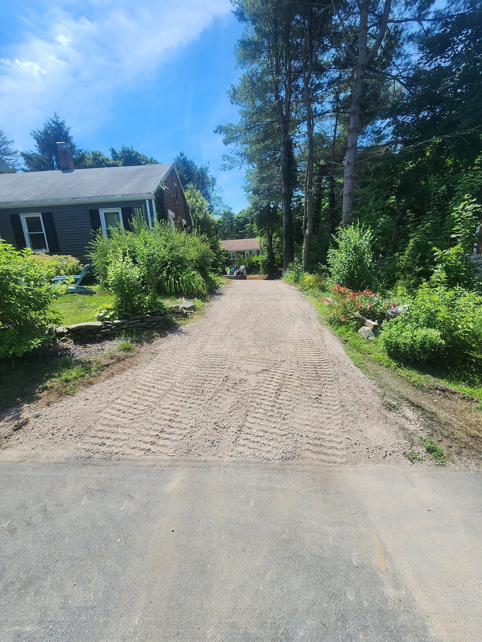 A gravel driveway leading to a house surrounded by trees on a sunny day.