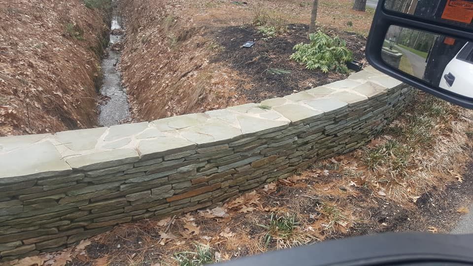 A car is driving down a road next to a stone wall.