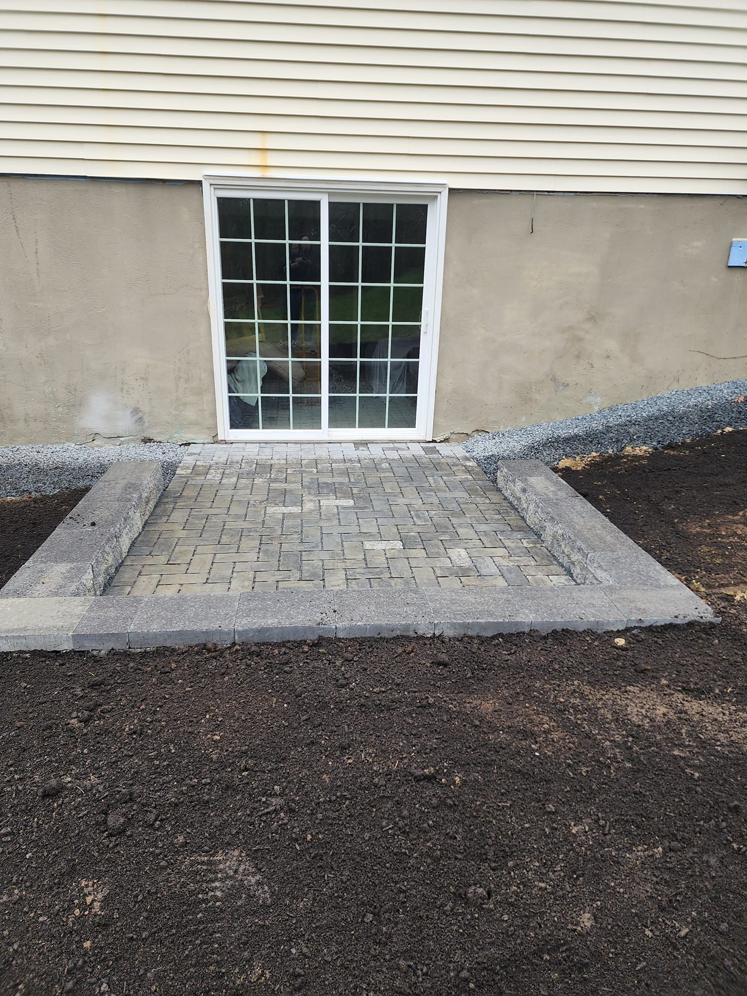 A window in the basement of a house with a brick walkway leading to it.
