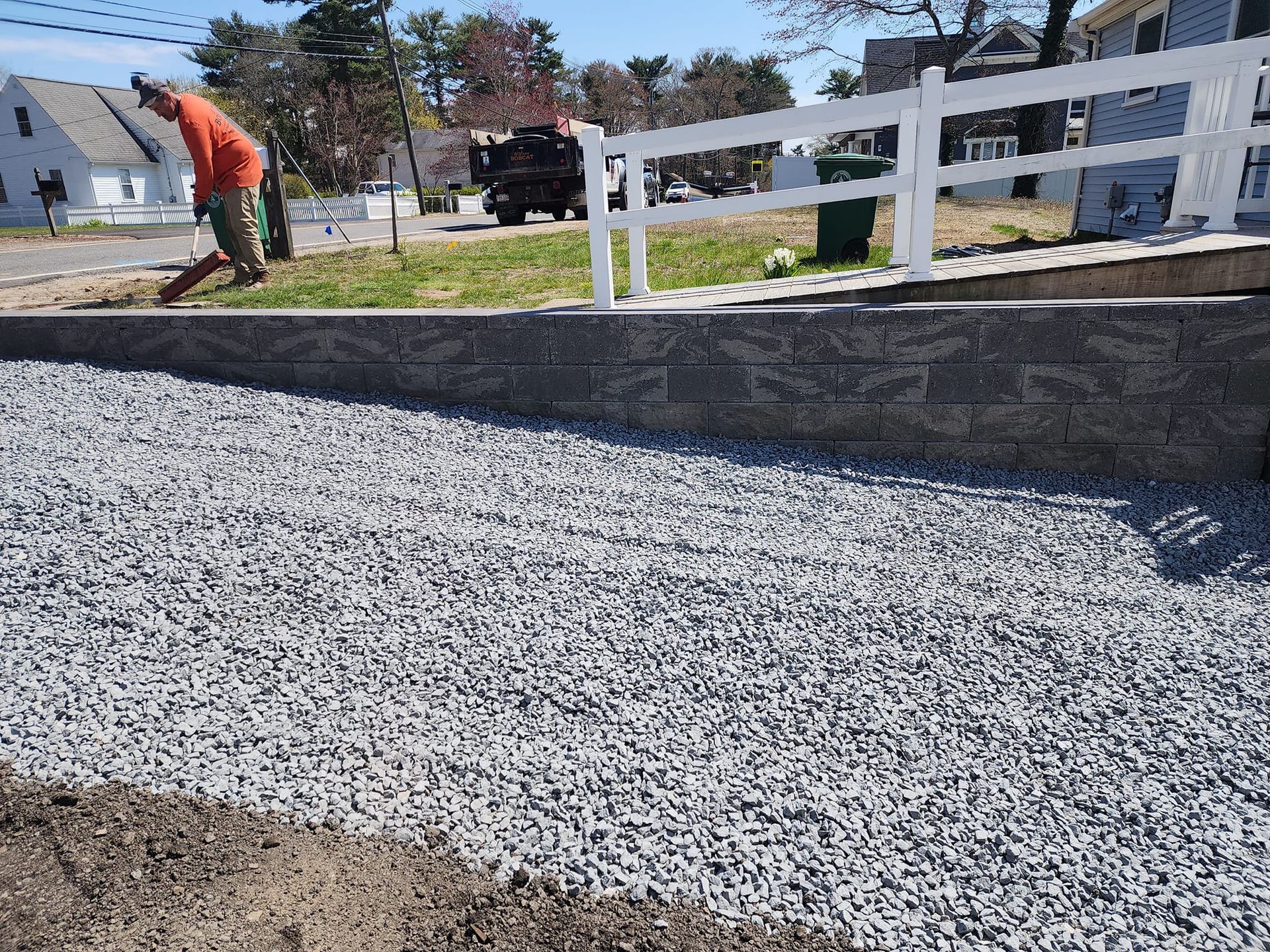 A man is working on a gravel driveway next to a fence.