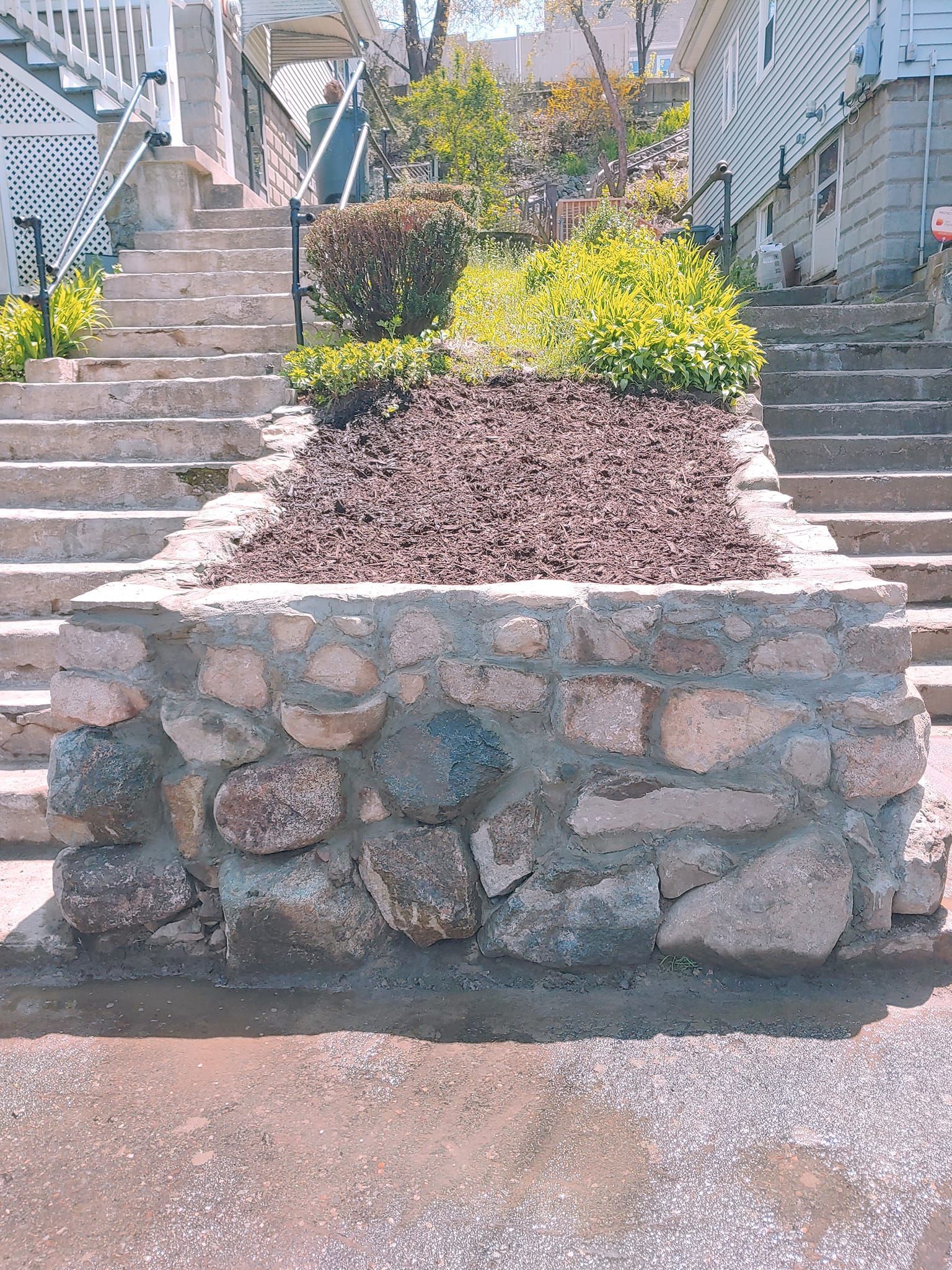 A stone wall with a garden in the middle of it next to stairs.
