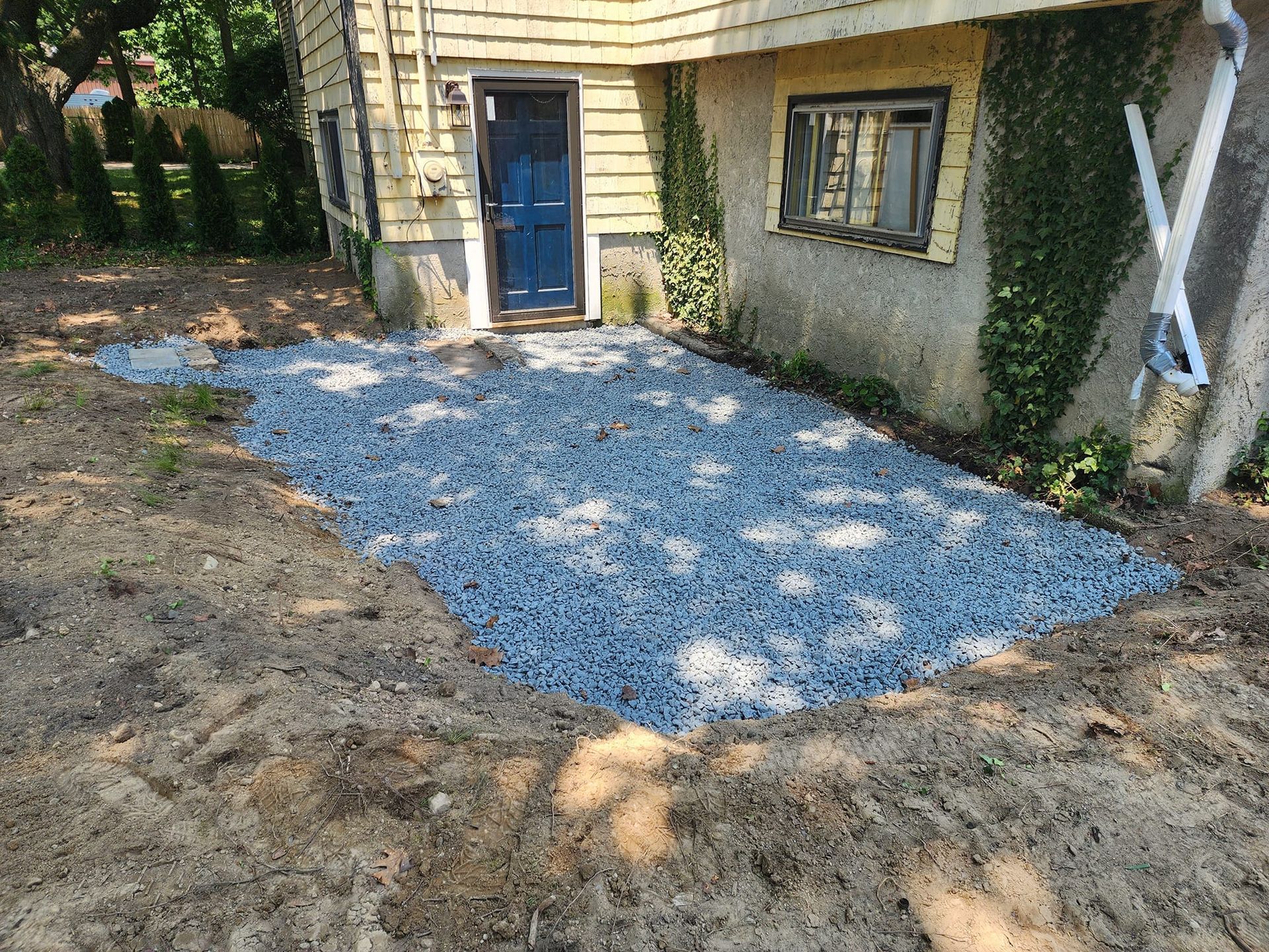 A house with a blue door and a gravel driveway in front of it.