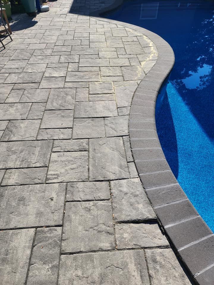 A patio next to a swimming pool with a brick walkway