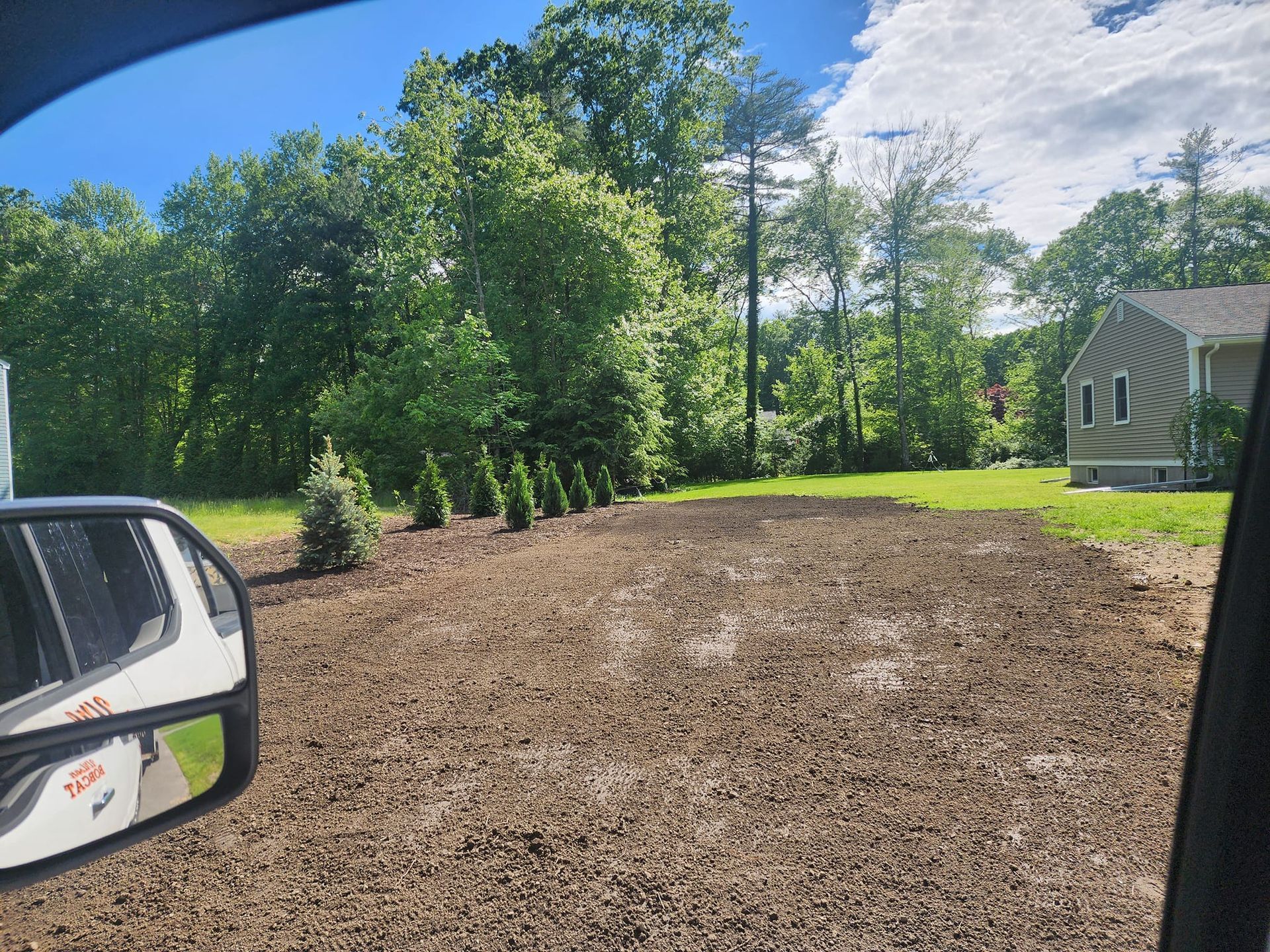 A car is driving down a dirt road next to a house.
