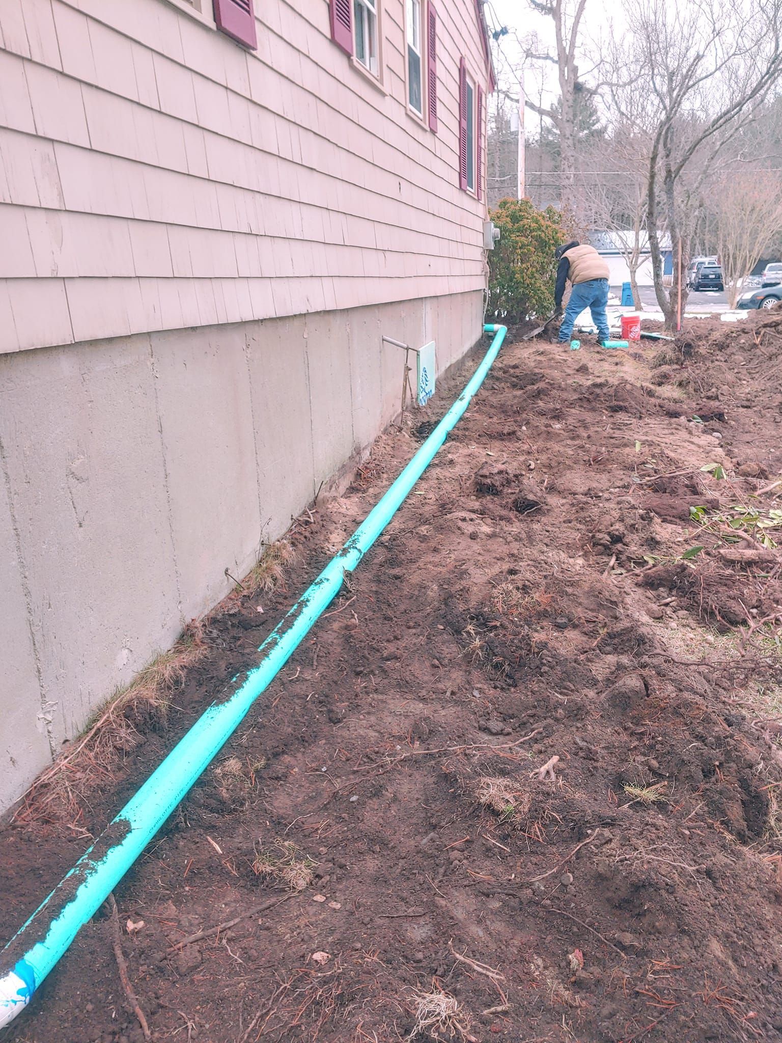 A man is digging in the dirt next to a house with a blue pipe.