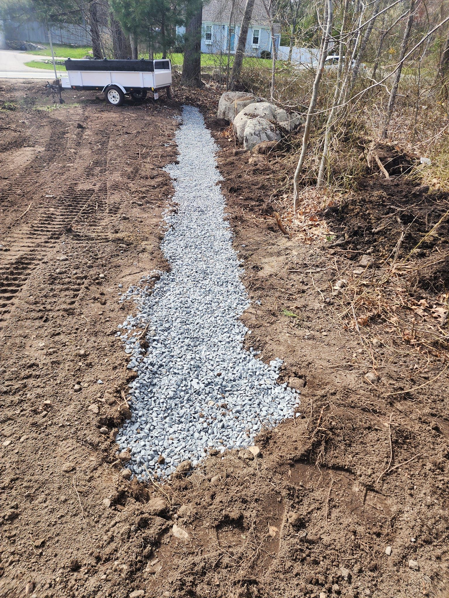 A white trailer is parked in the dirt next to a stream of gravel.