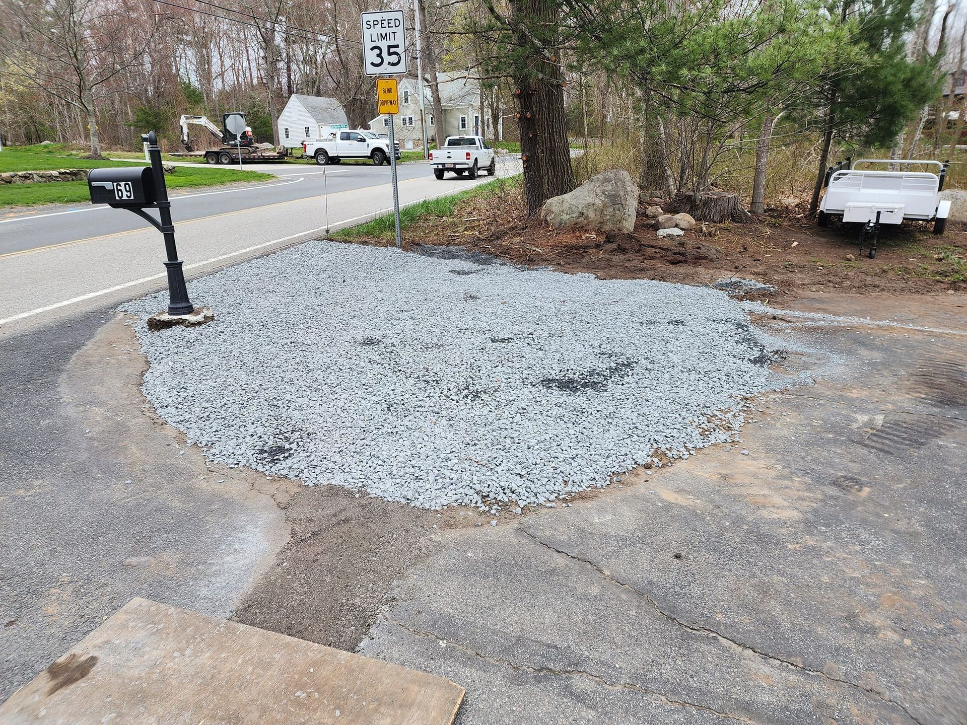 A mailbox is sitting in the middle of a gravel area next to a road.