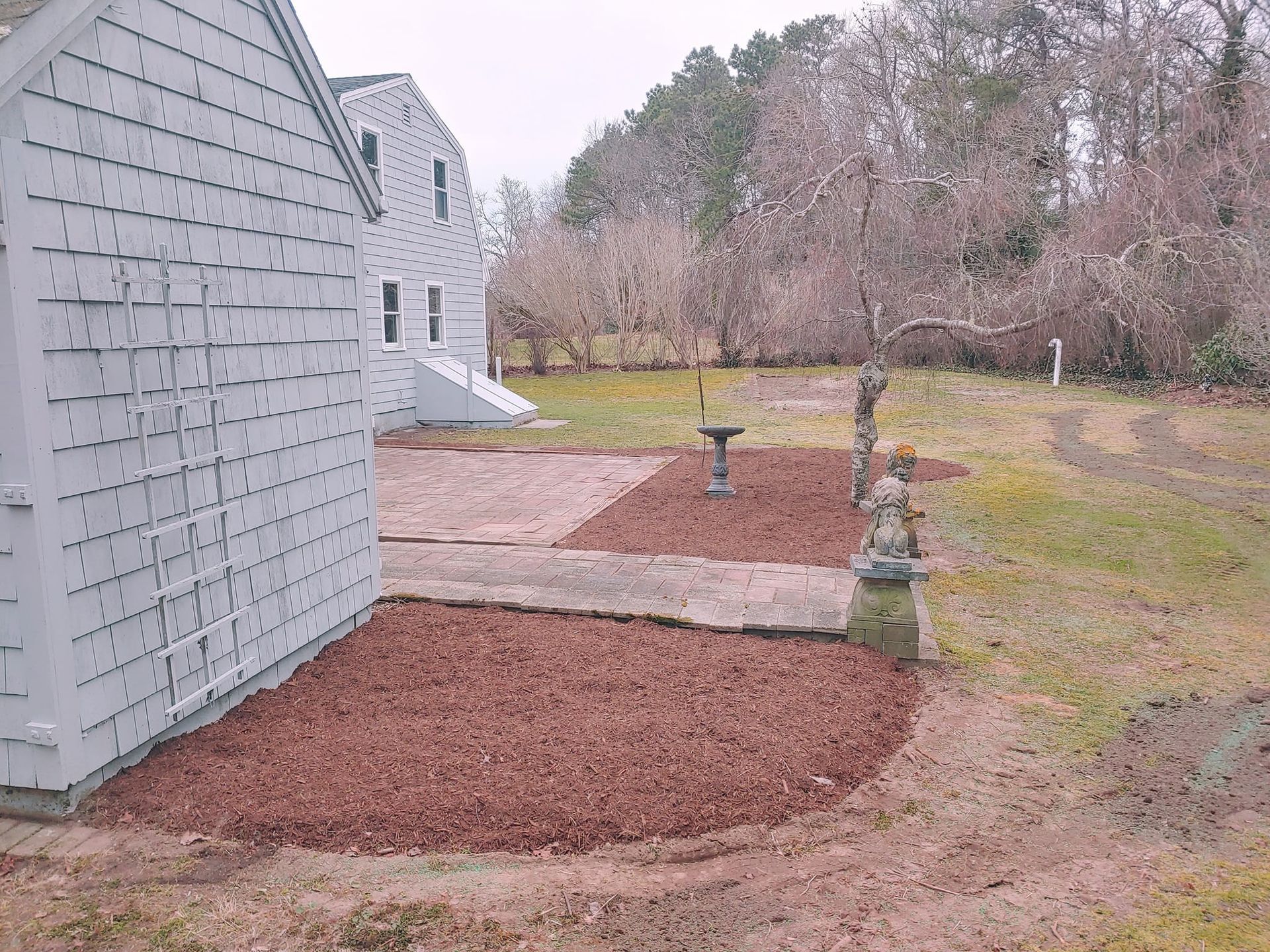 There is a bird bath in the middle of the yard next to a house.