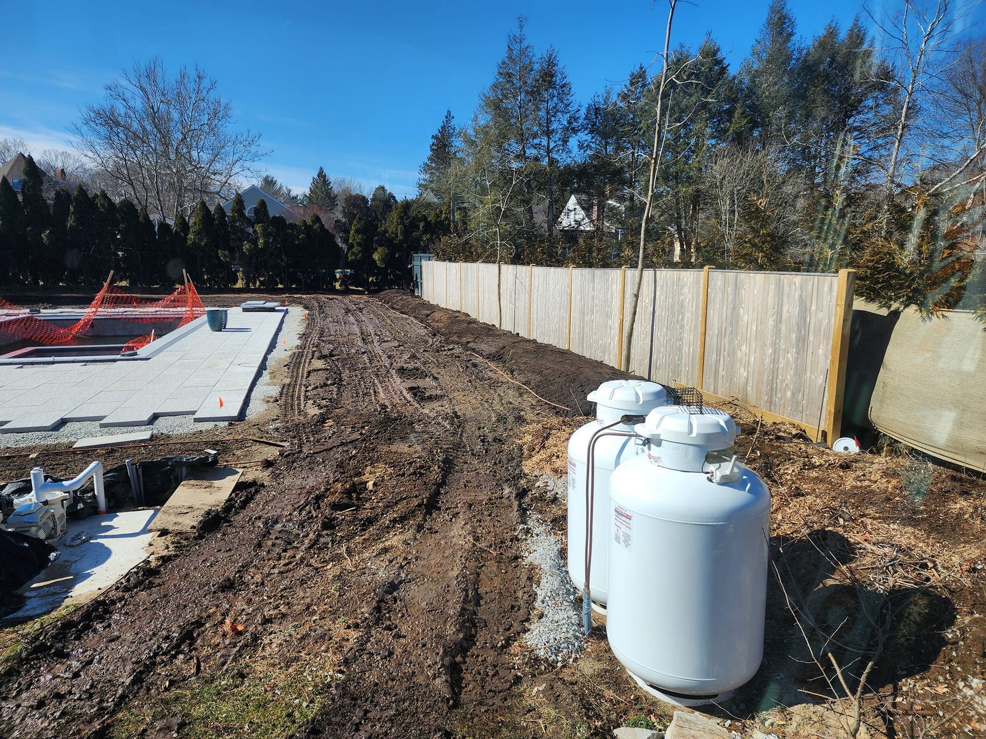 Two propane tanks are sitting in the dirt next to a wooden fence.