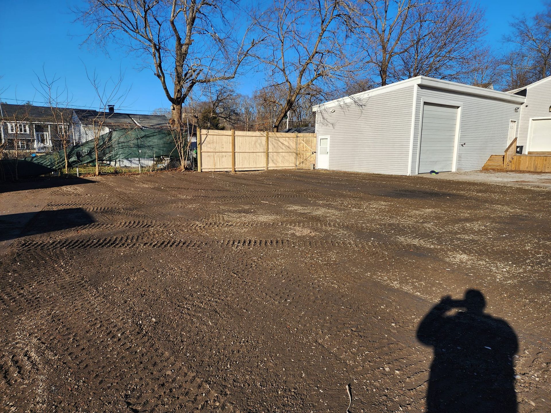 A man is taking a picture of a dirt field with a shed in the background.