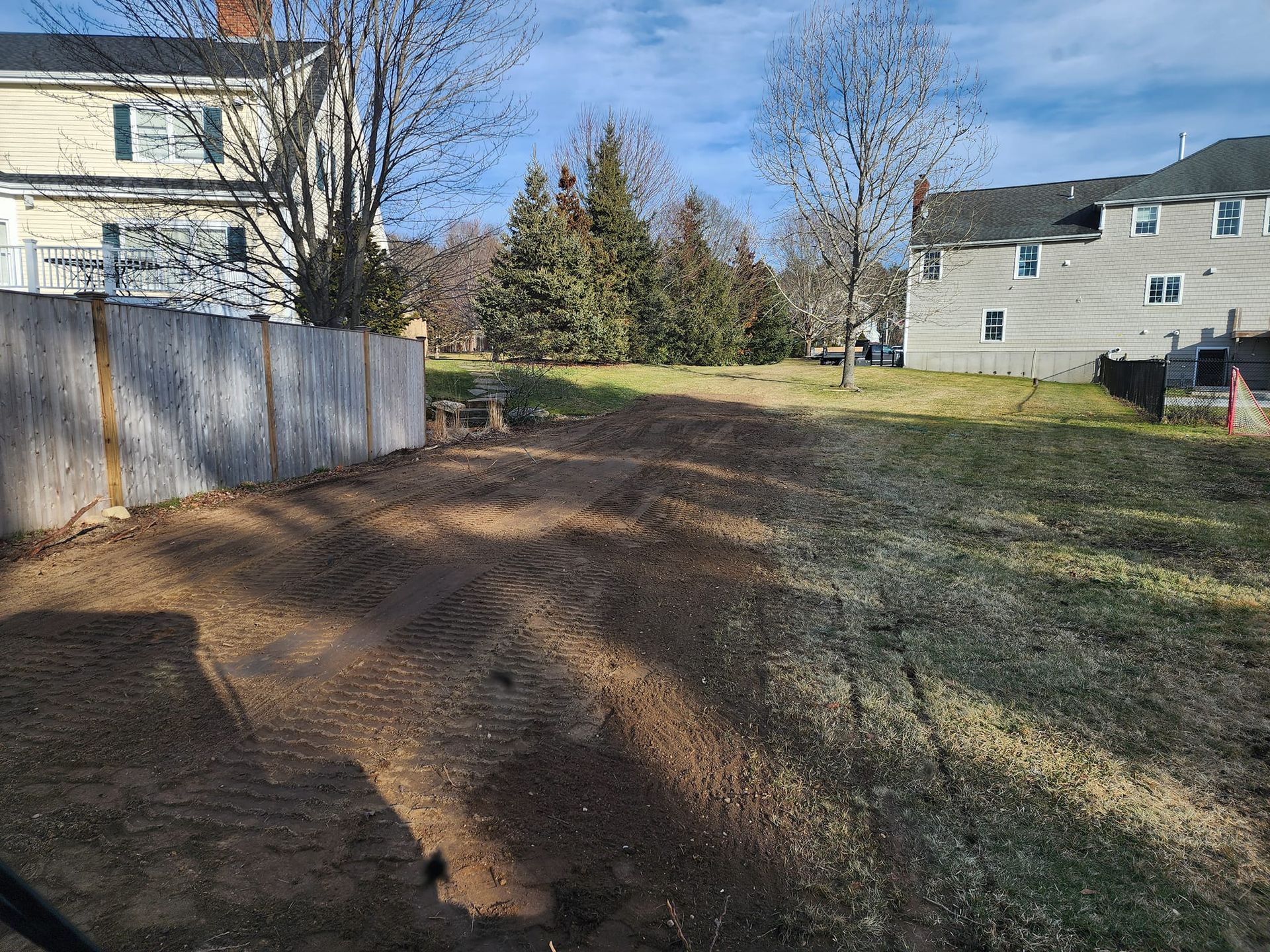 A dirt road leading to a house with a fence in the background.