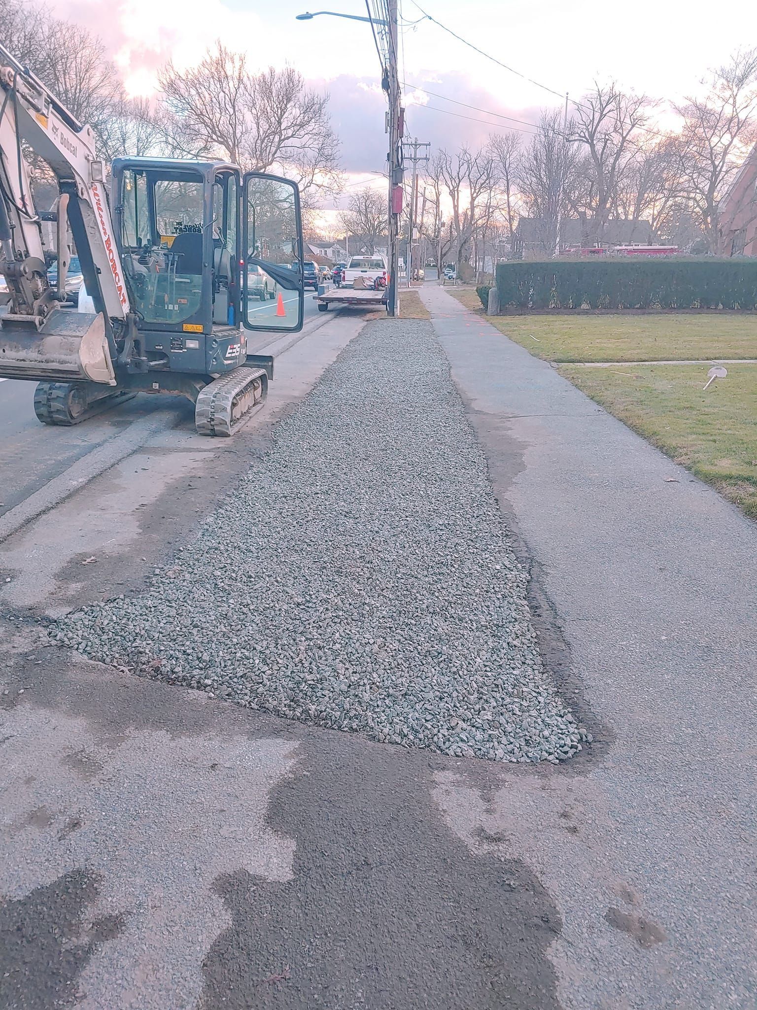 A small excavator is laying gravel on the side of a road.