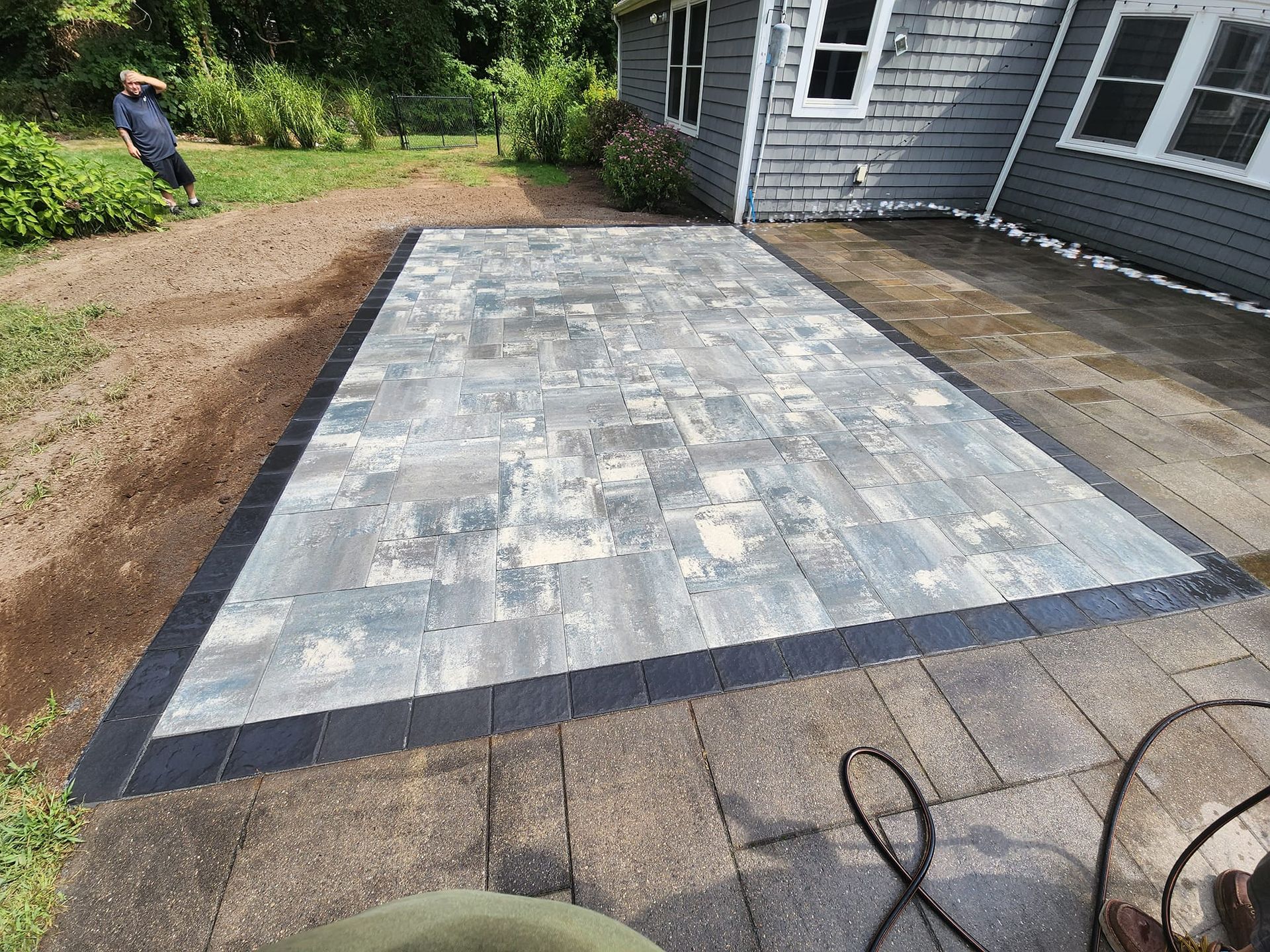 A patio with a black border is being built in front of a house.