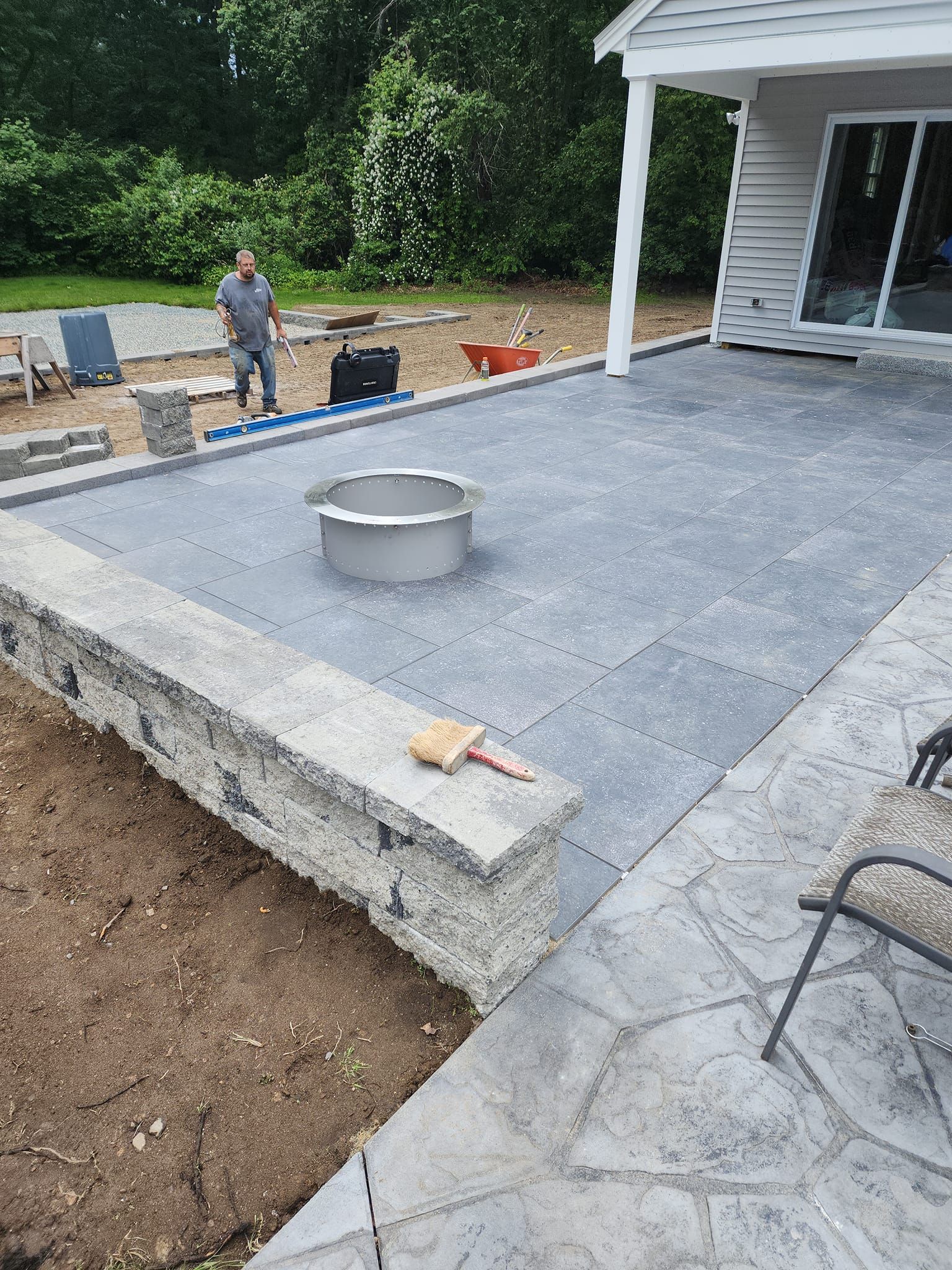 A man is standing on a patio with a fire pit in the middle of it.