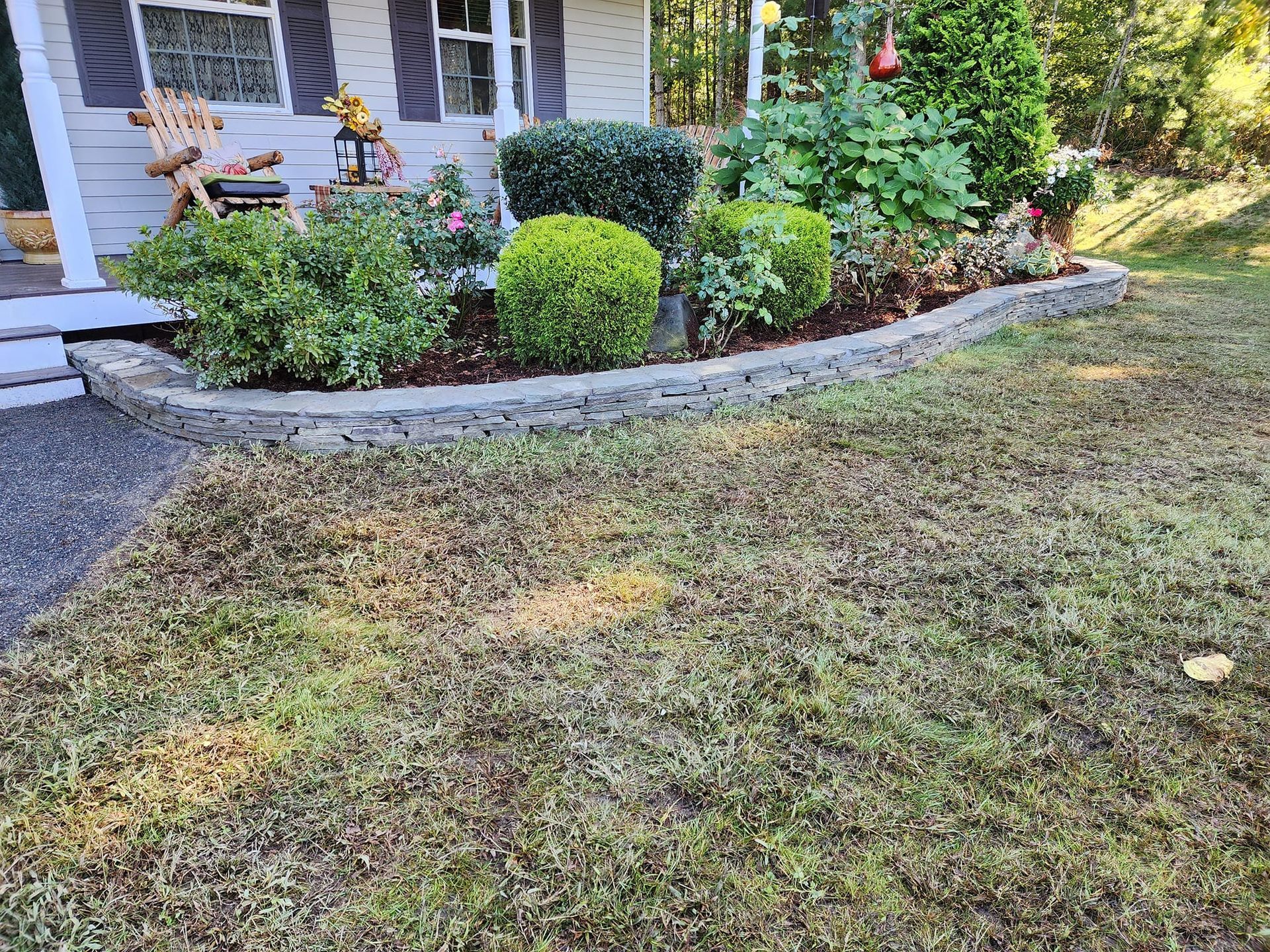 A lush green lawn in front of a house with flowers and bushes.