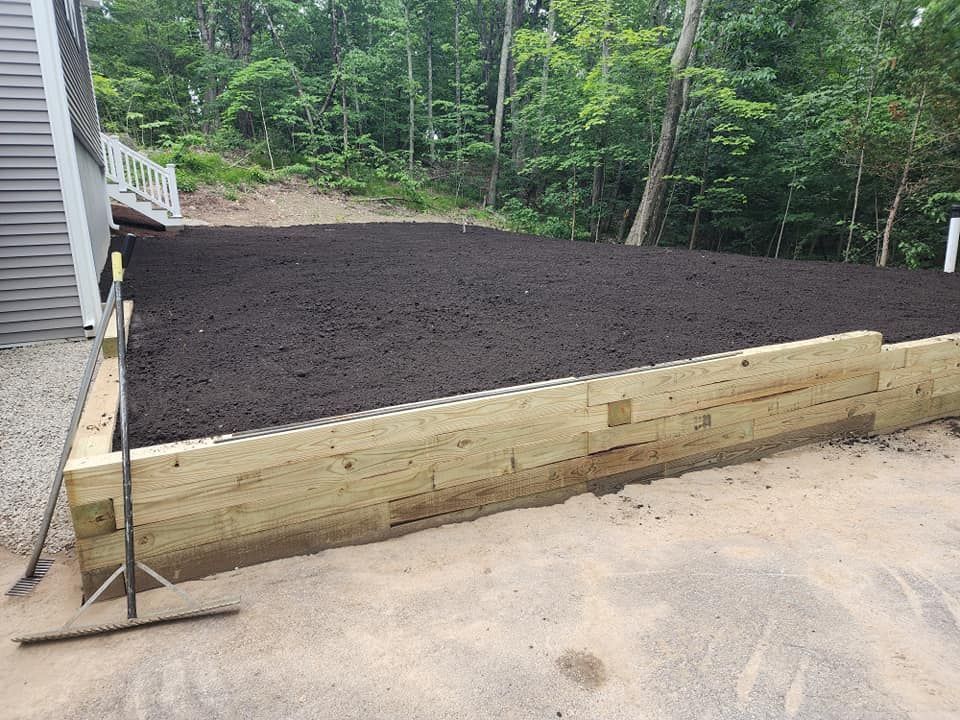 A wooden retaining wall is surrounded by dirt and trees.