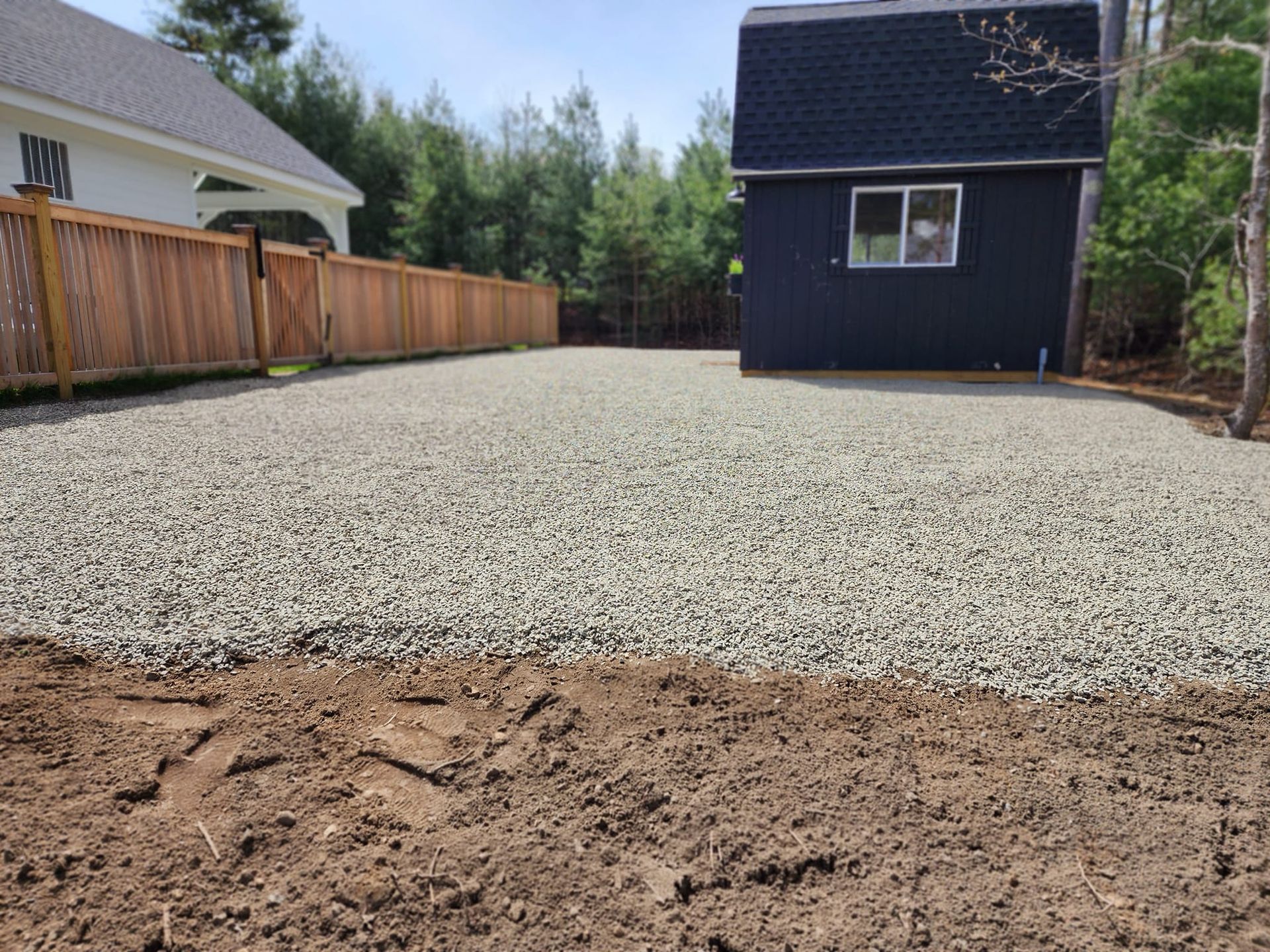 A gravel driveway leading to a house with a wooden fence.