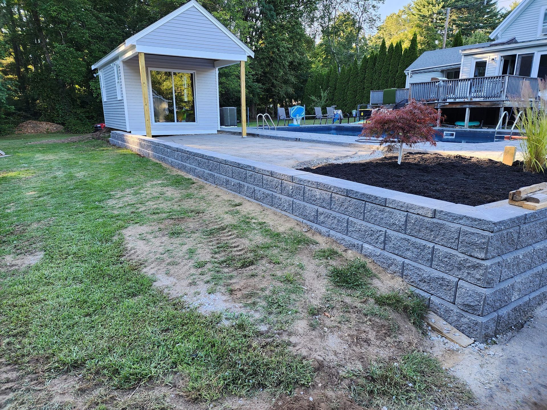 A brick wall is being built in the backyard of a house next to a pool.