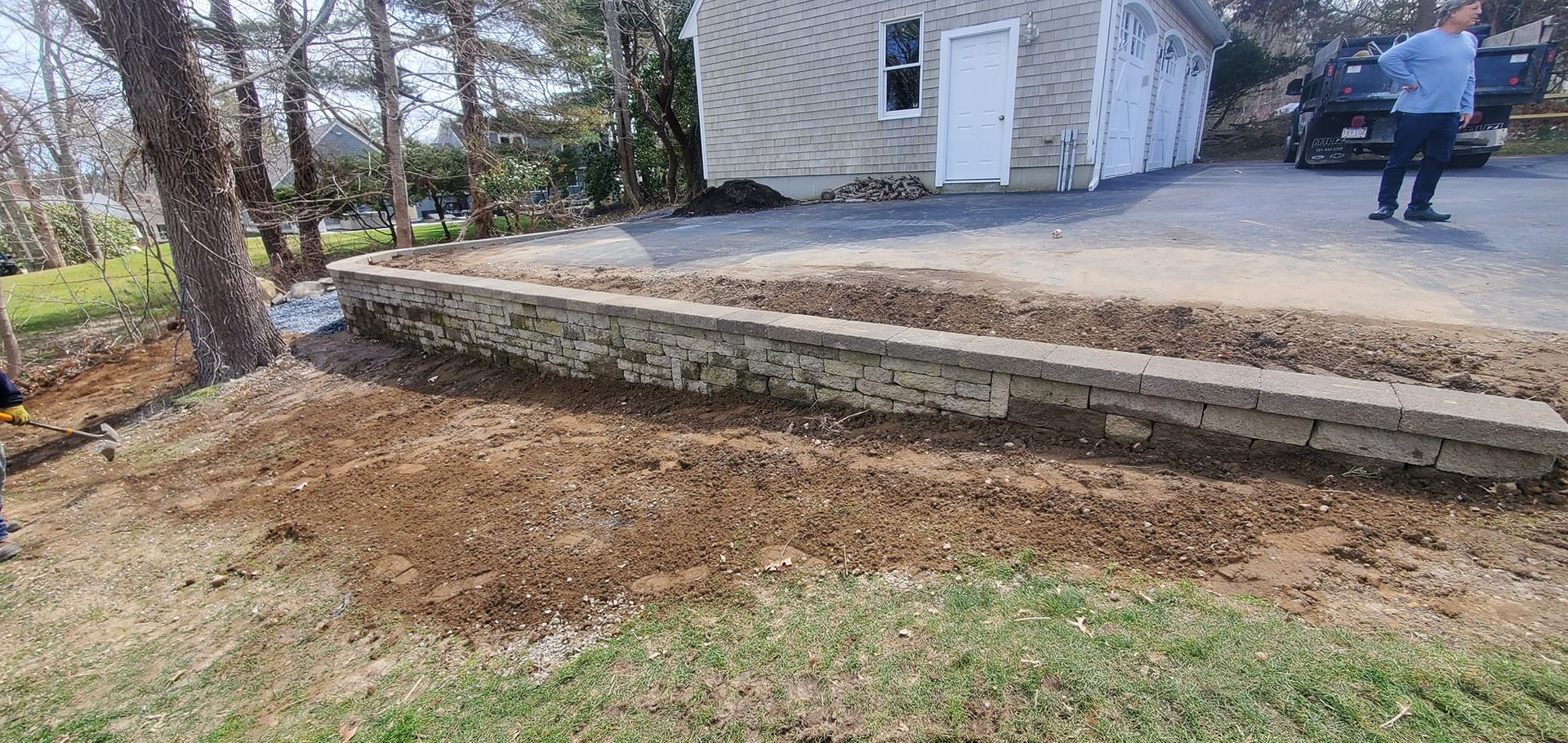 A man is standing in front of a house with a truck parked in the driveway.