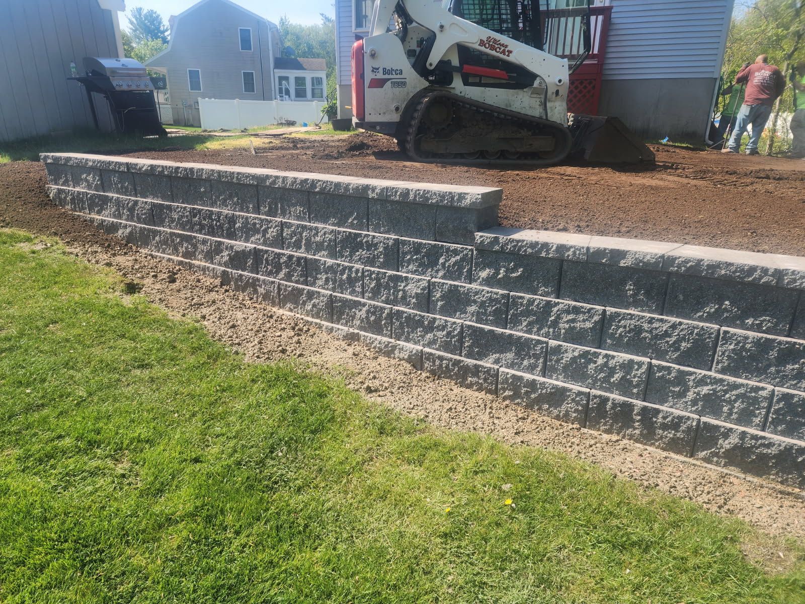 A bulldozer is moving dirt next to a brick wall.