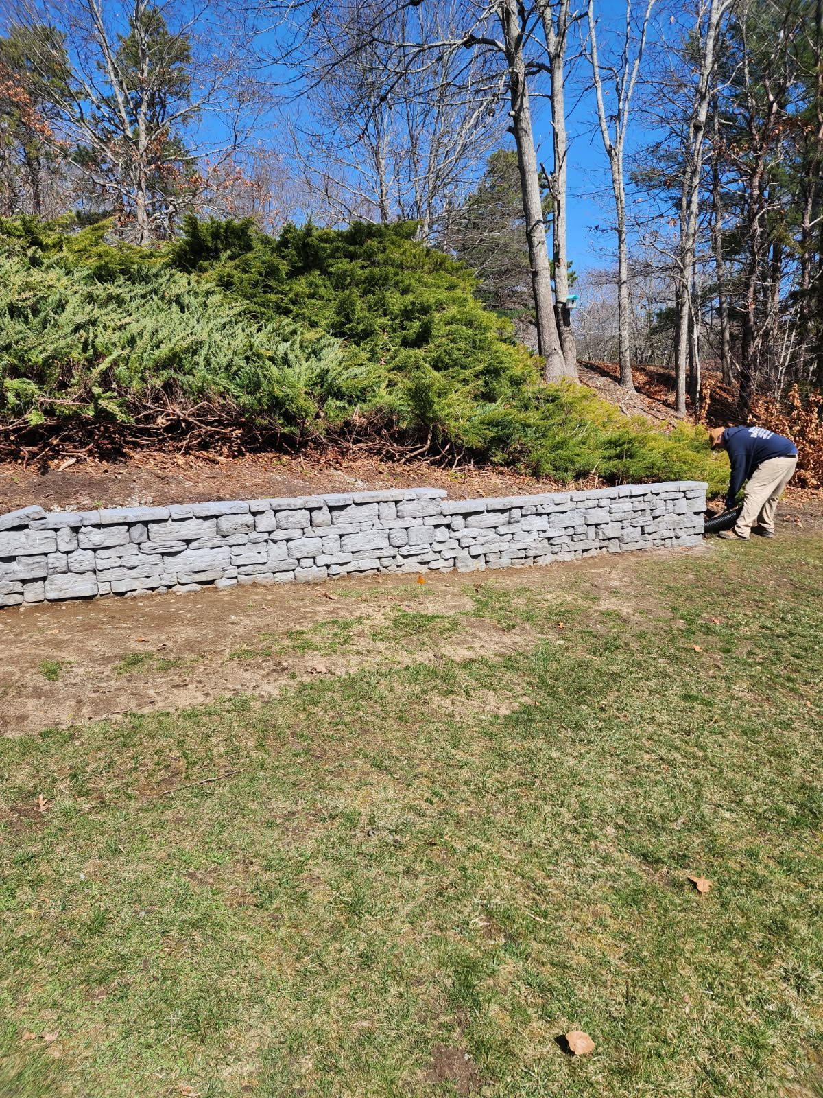 A man is working on a stone wall in a yard.