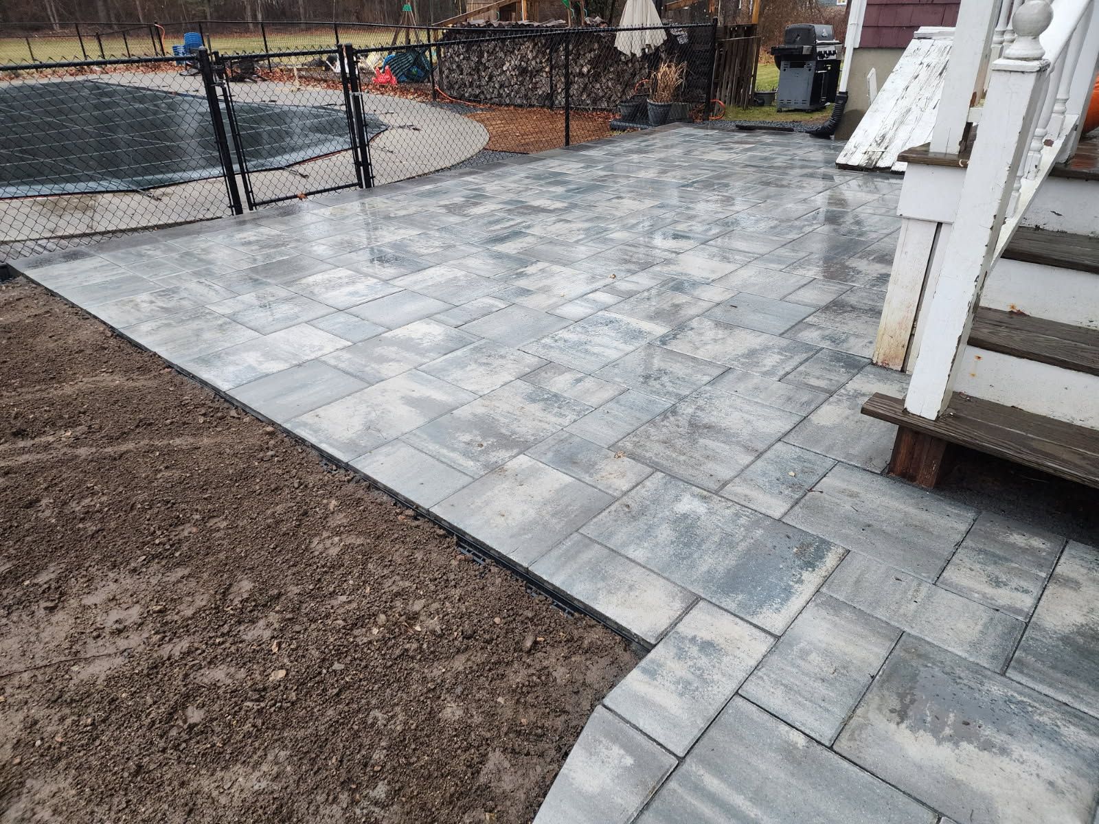 A patio with stairs and a pool in the background.