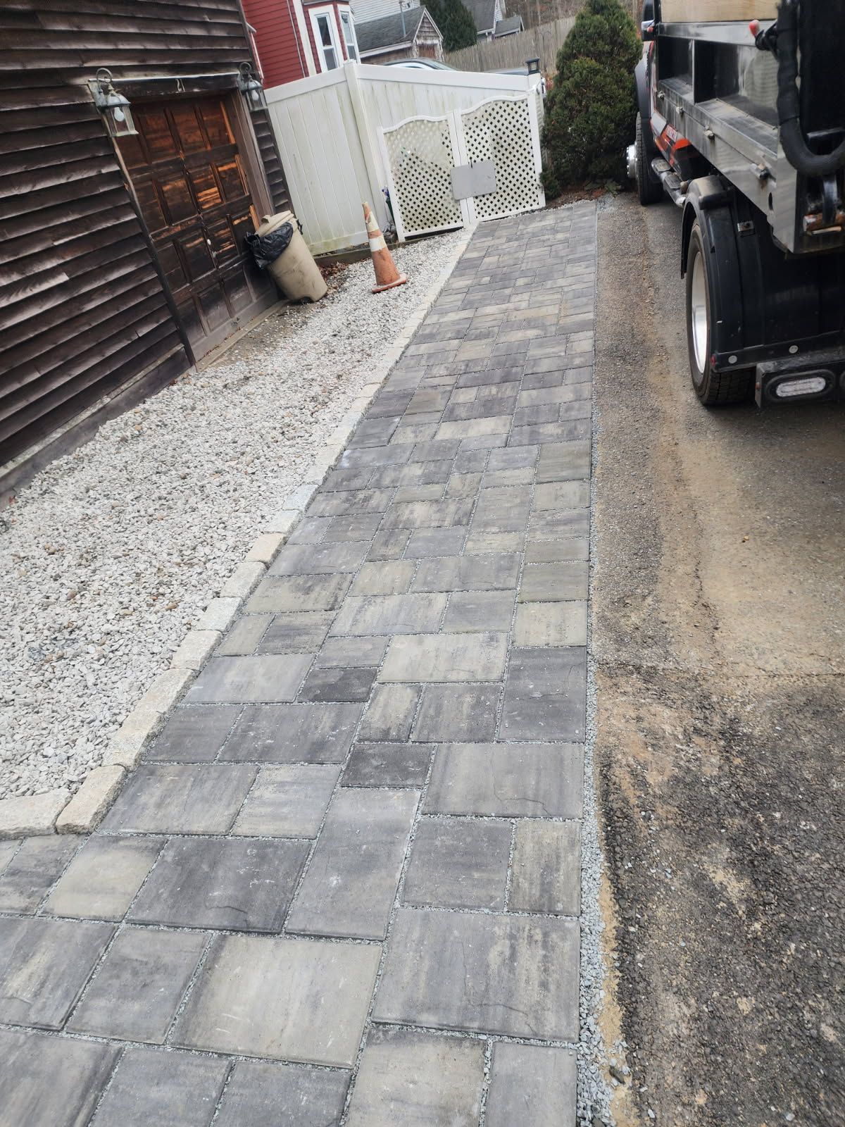 A truck is parked on the side of the road next to a brick walkway.