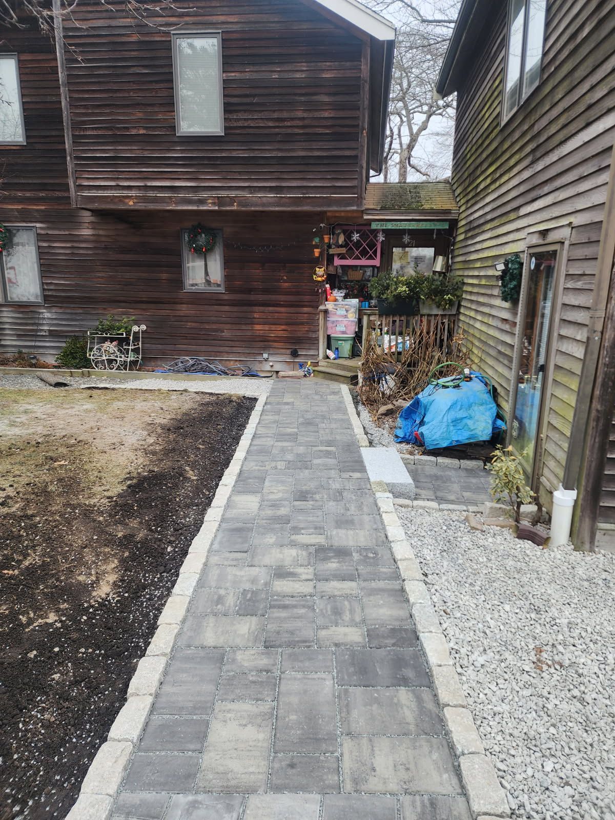 A brick walkway leading to a house with a wooden house in the background.