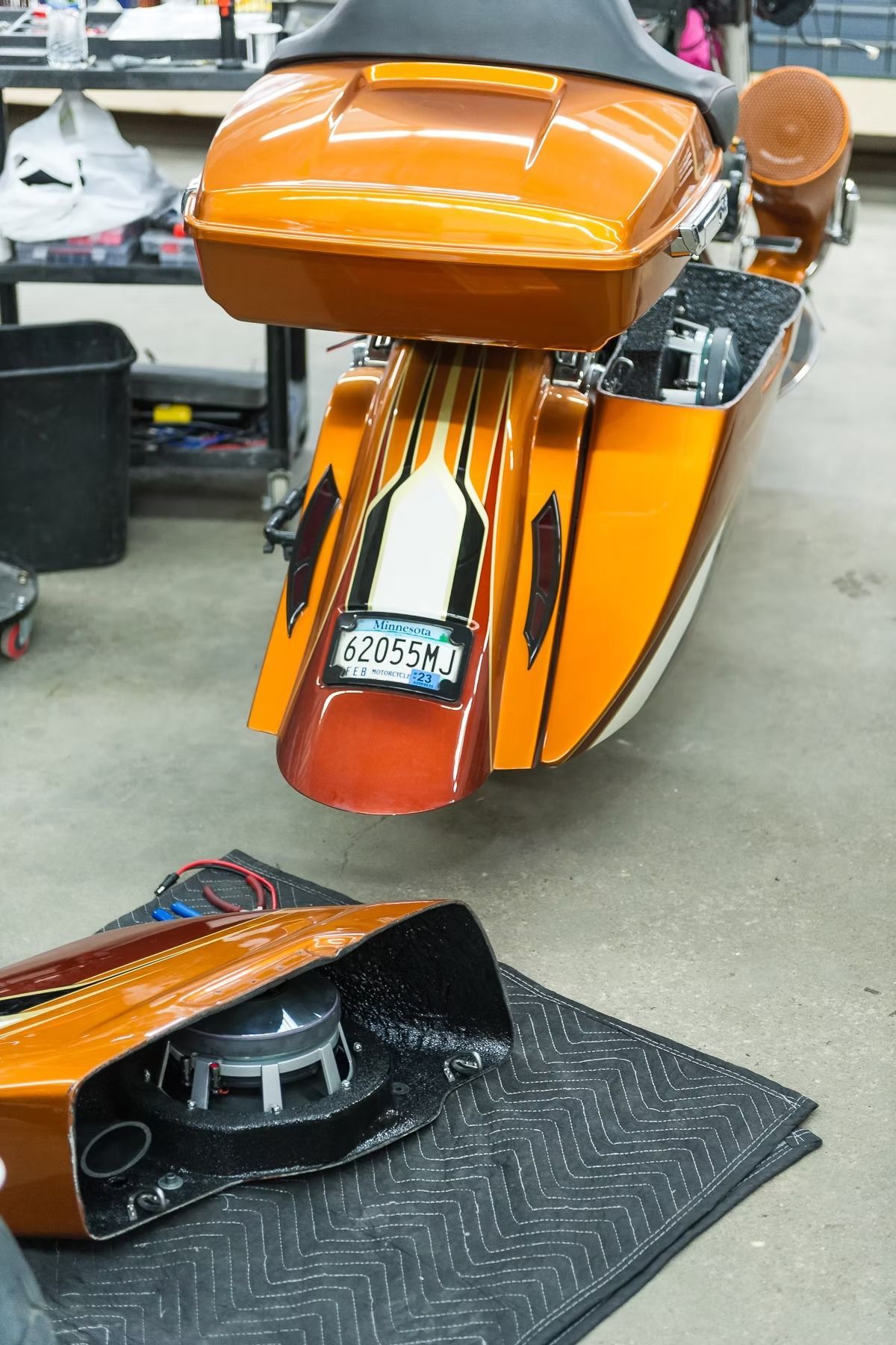 Orange custom motorcycle fairing and front end in a workshop, with a detached black part in the foreground
