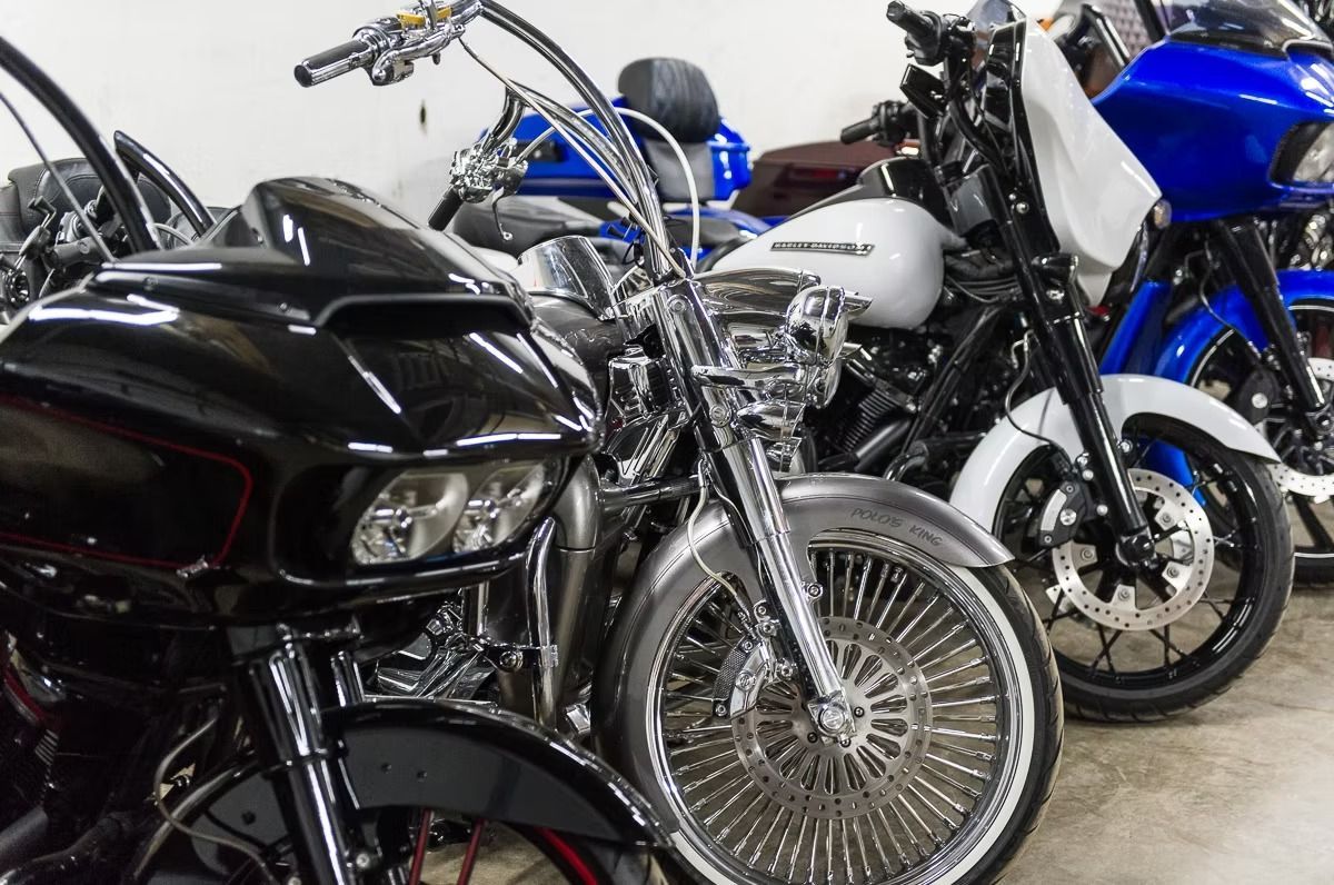 Several custom motorcycles parked indoors, including a black bike in front and blue and silver bikes behind.