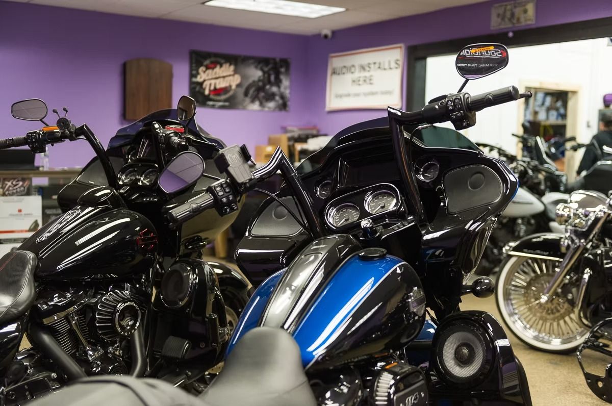 Several motorcycles parked indoors in a showroom, including black and blue bikes against purple walls.