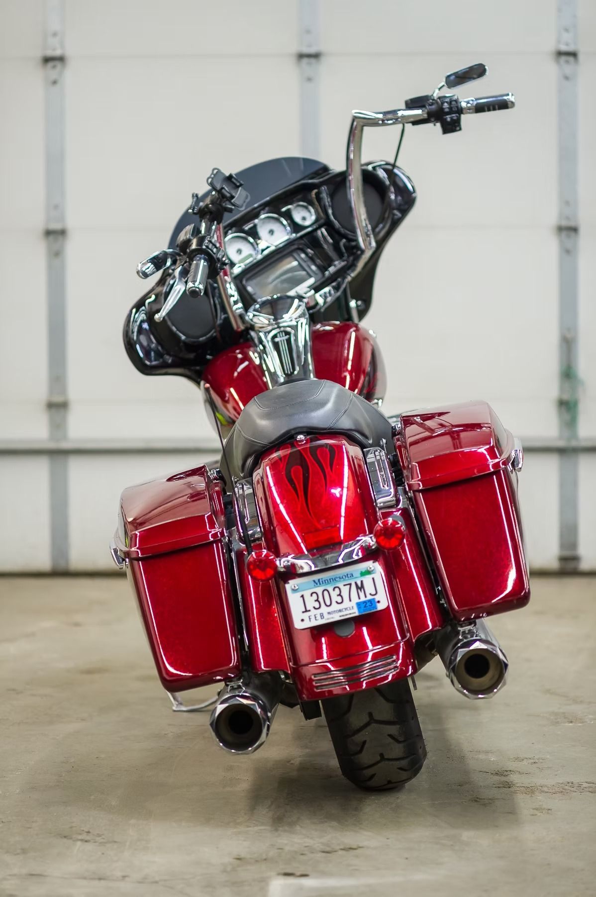 Rear view of a red touring motorcycle with saddlebags, parked indoors on a concrete floor.