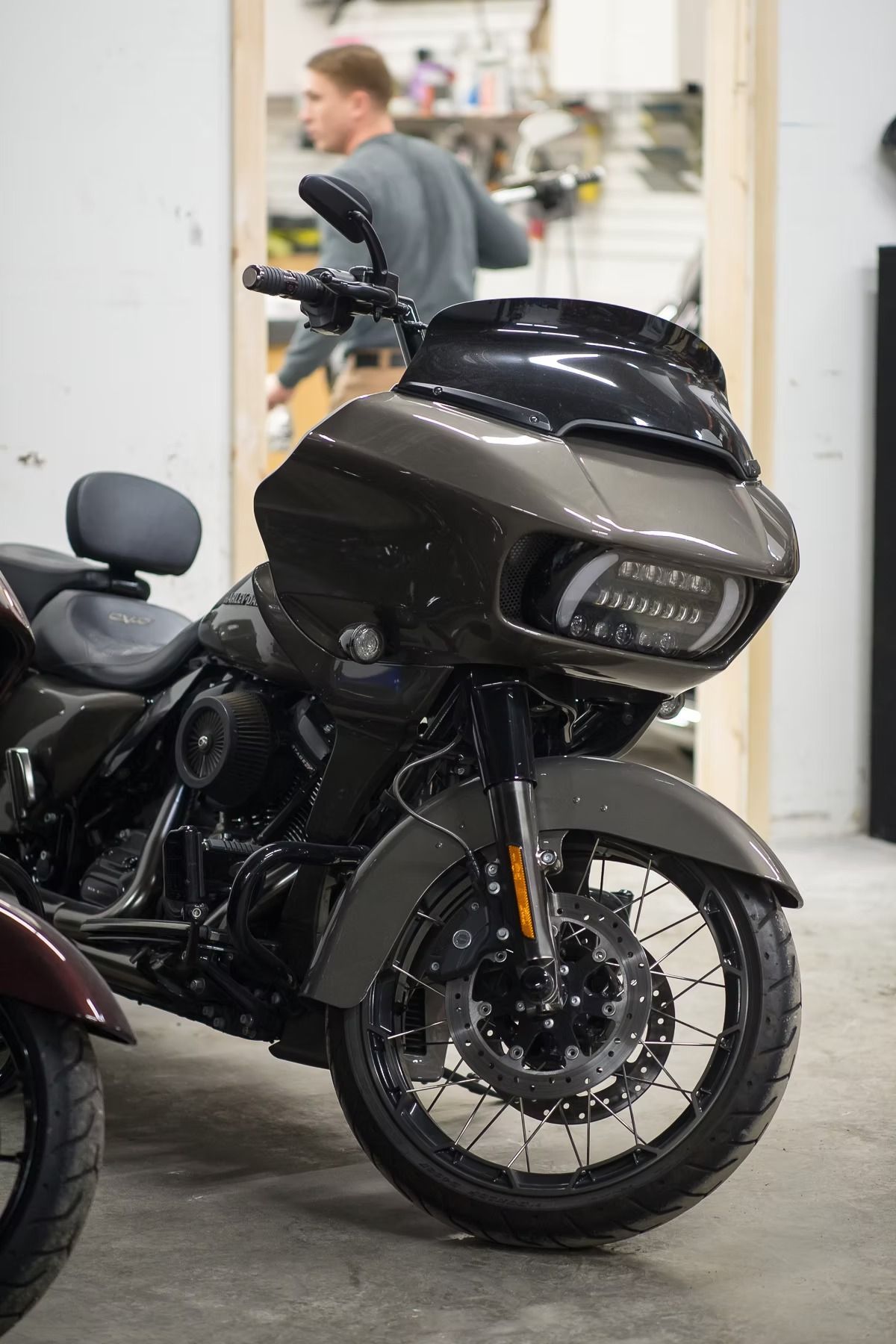 Black touring motorcycle parked indoors, with a person blurred in the background.