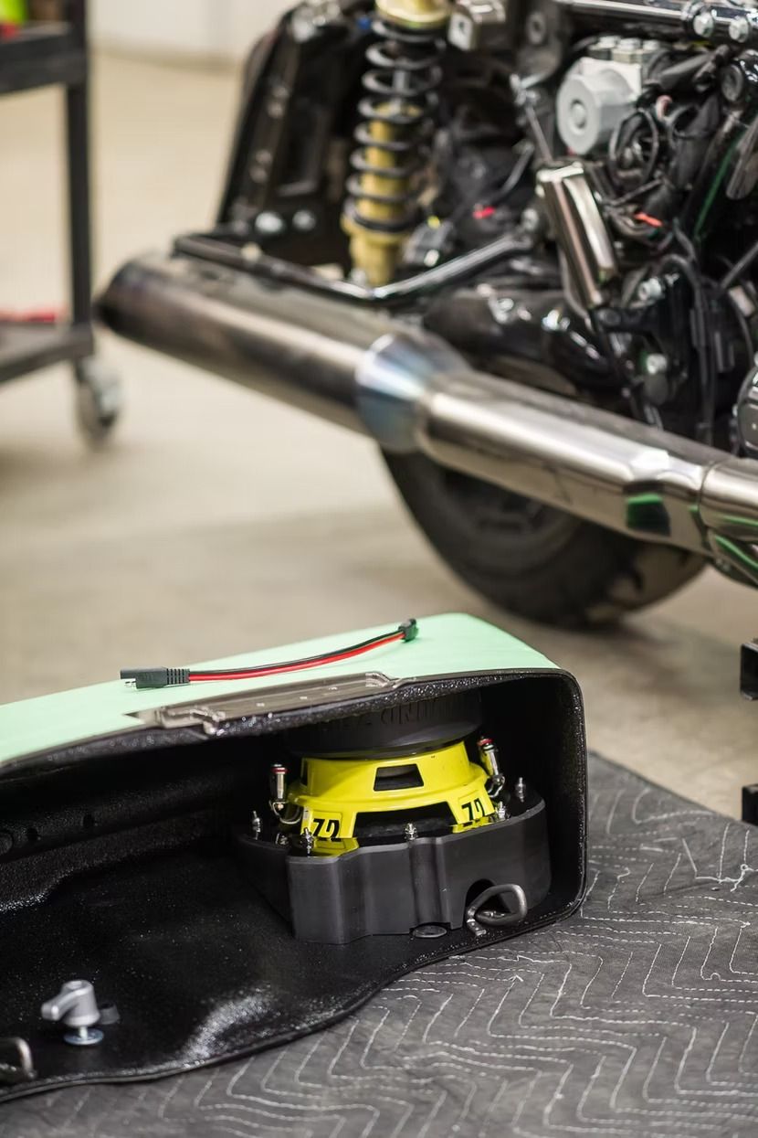 Yellow engine component under a motorcycle’s chrome exhaust in a workshop with a cutaway black casing
