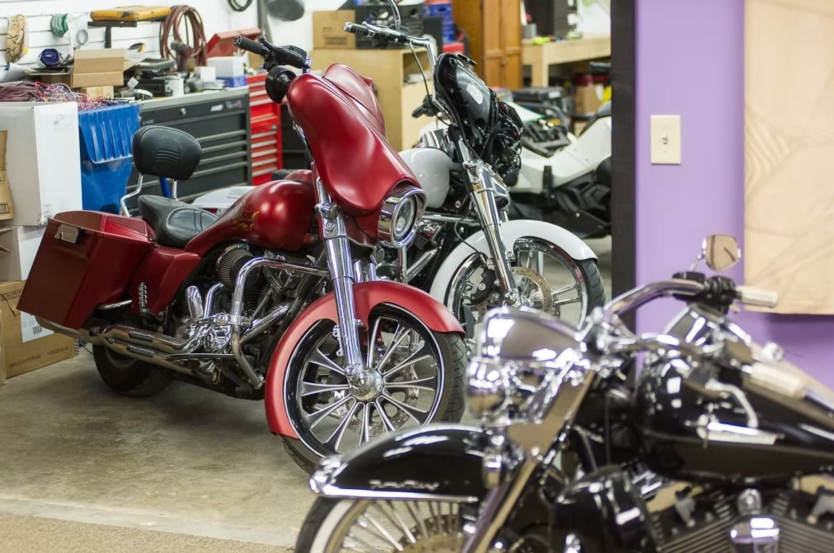 Red custom motorcycle in a garage with other bikes and workshop tools in the background