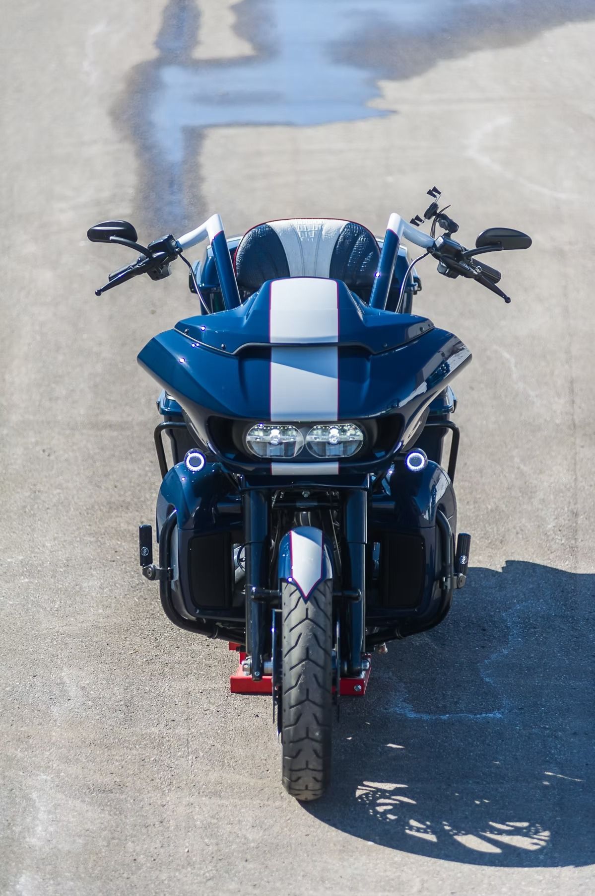 Blue three-wheeled motorcycle parked on pavement, viewed from the front.