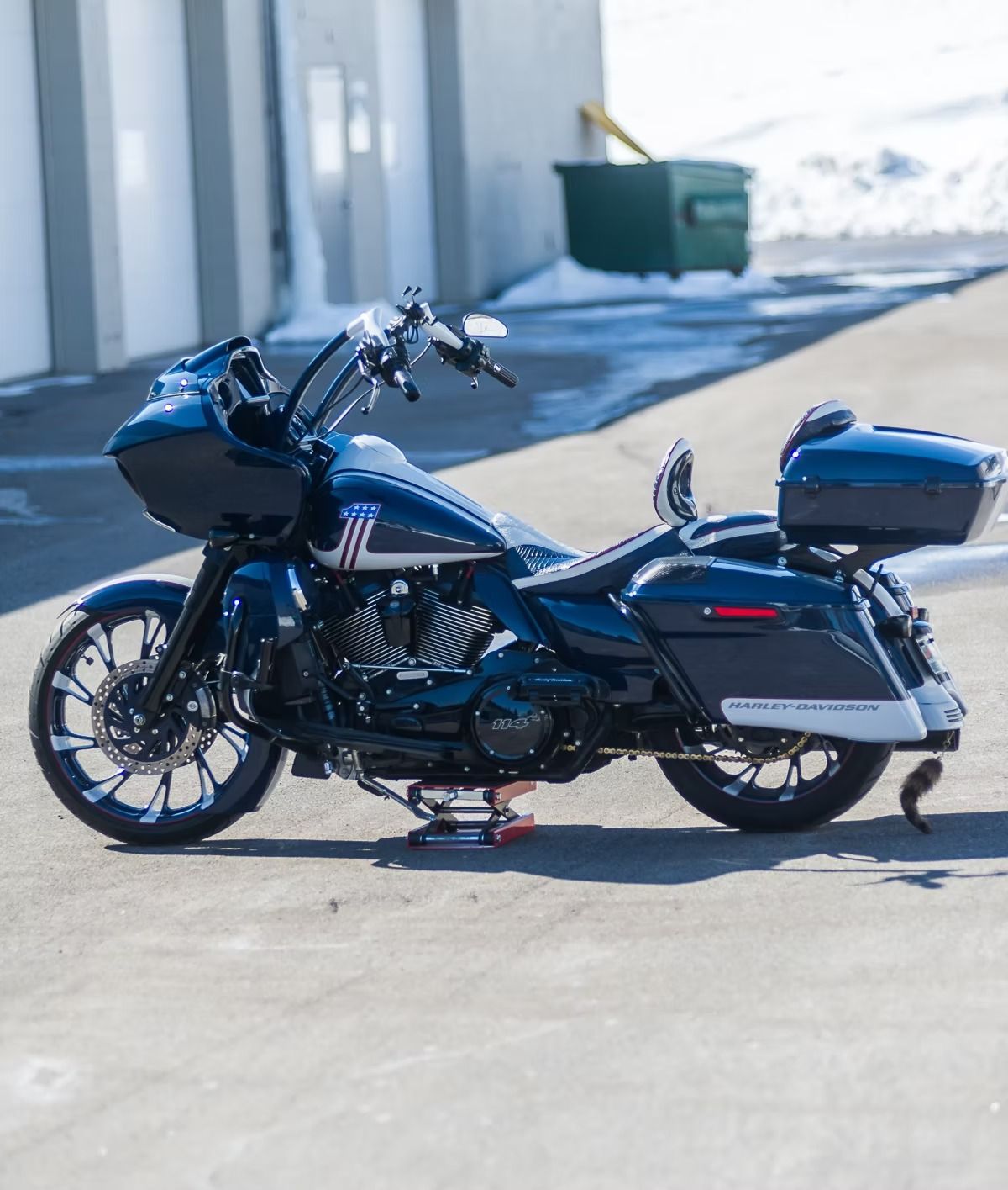 Black touring motorcycle parked on a sunlit paved road with a green dumpster in the background